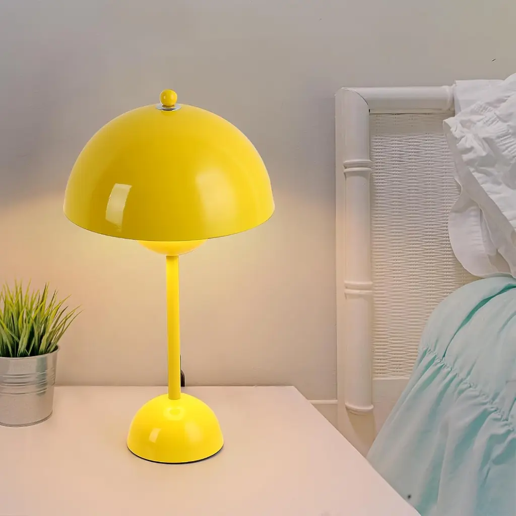 Una lámpara de escritorio amarilla con pantalla en forma de hongo en una mesita de noche.