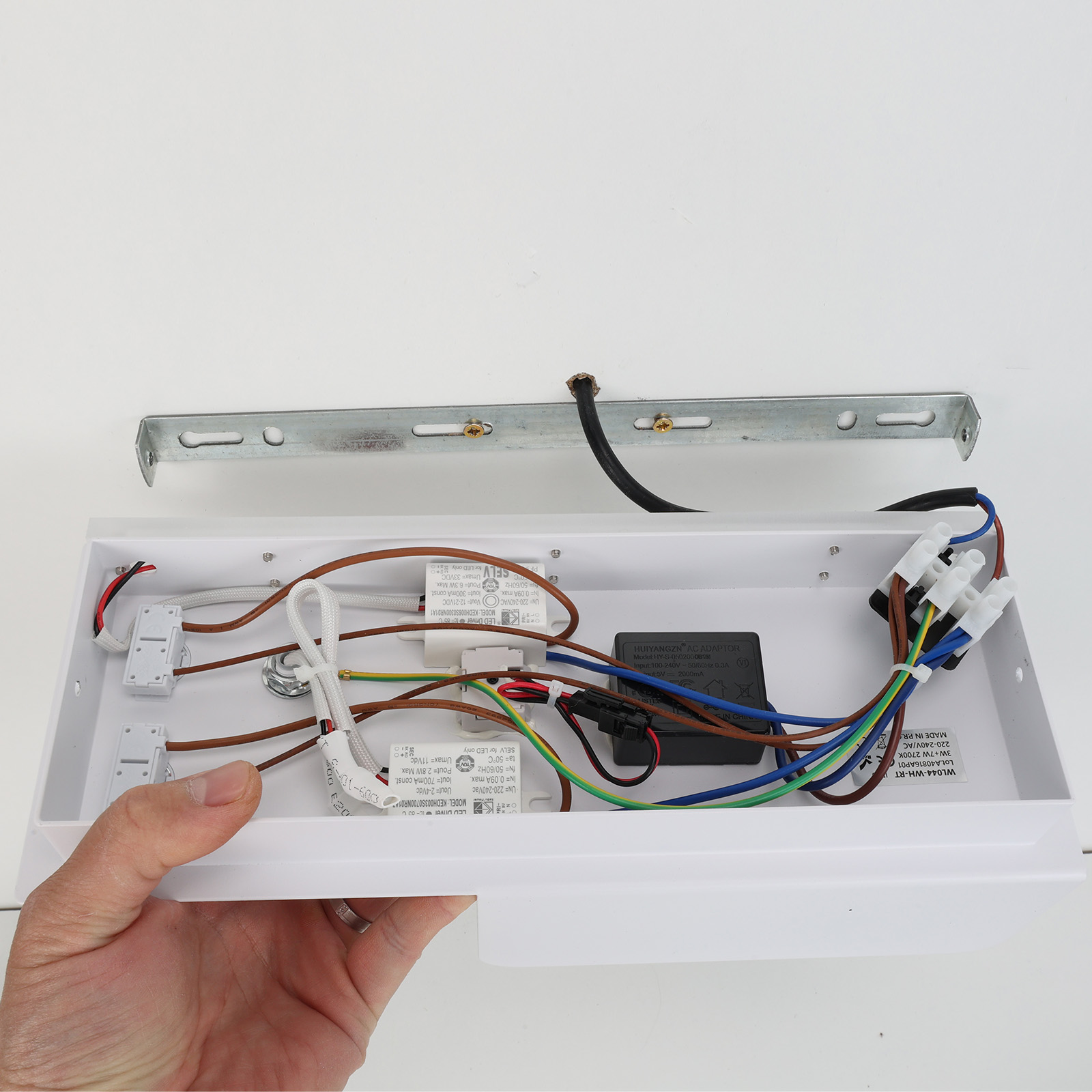 Una carcasa blanca con componentes eléctricos y cables. Una mano sujeta la carcasa.