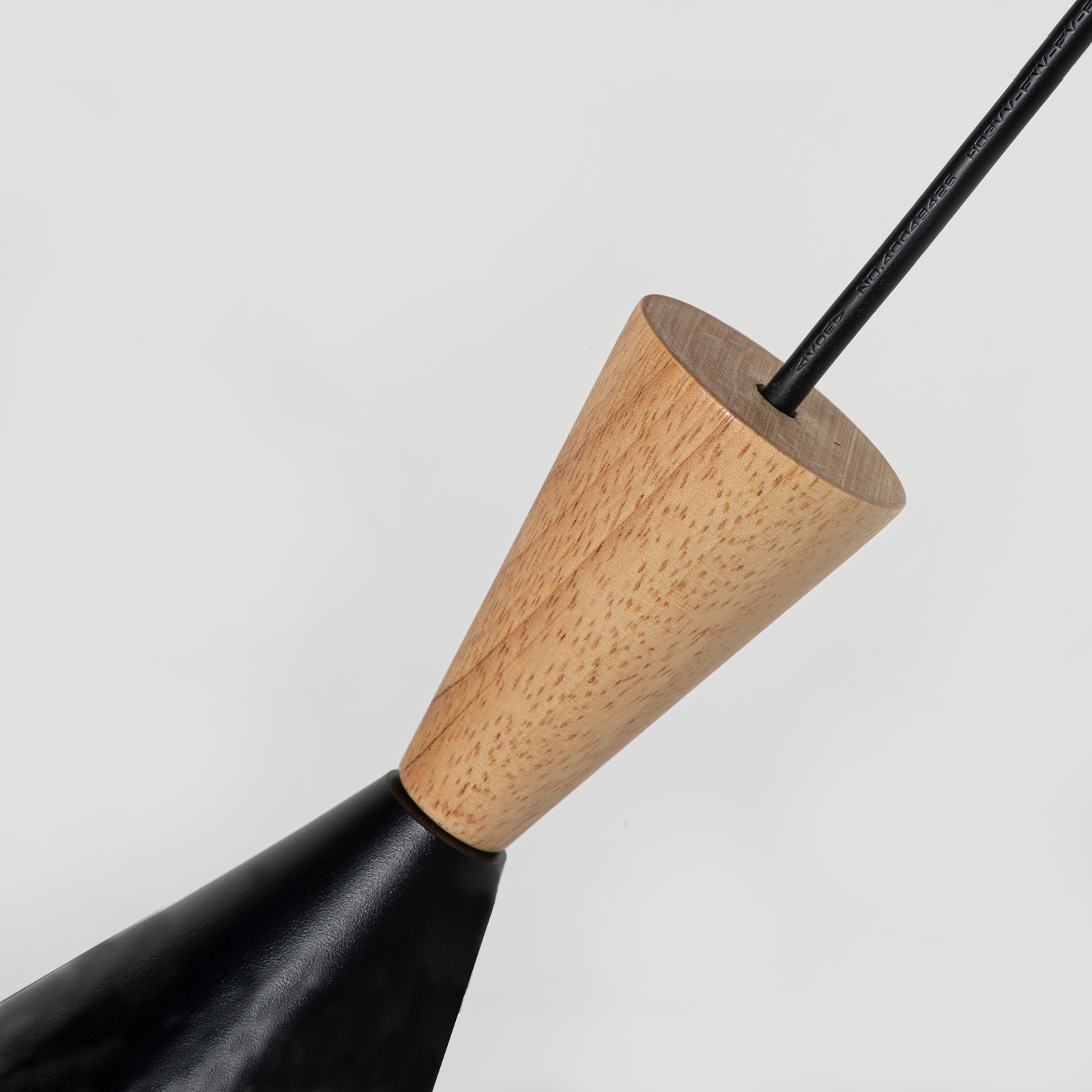 Un cable negro sale de un elemento cónico de madera unido a una lámpara negra.