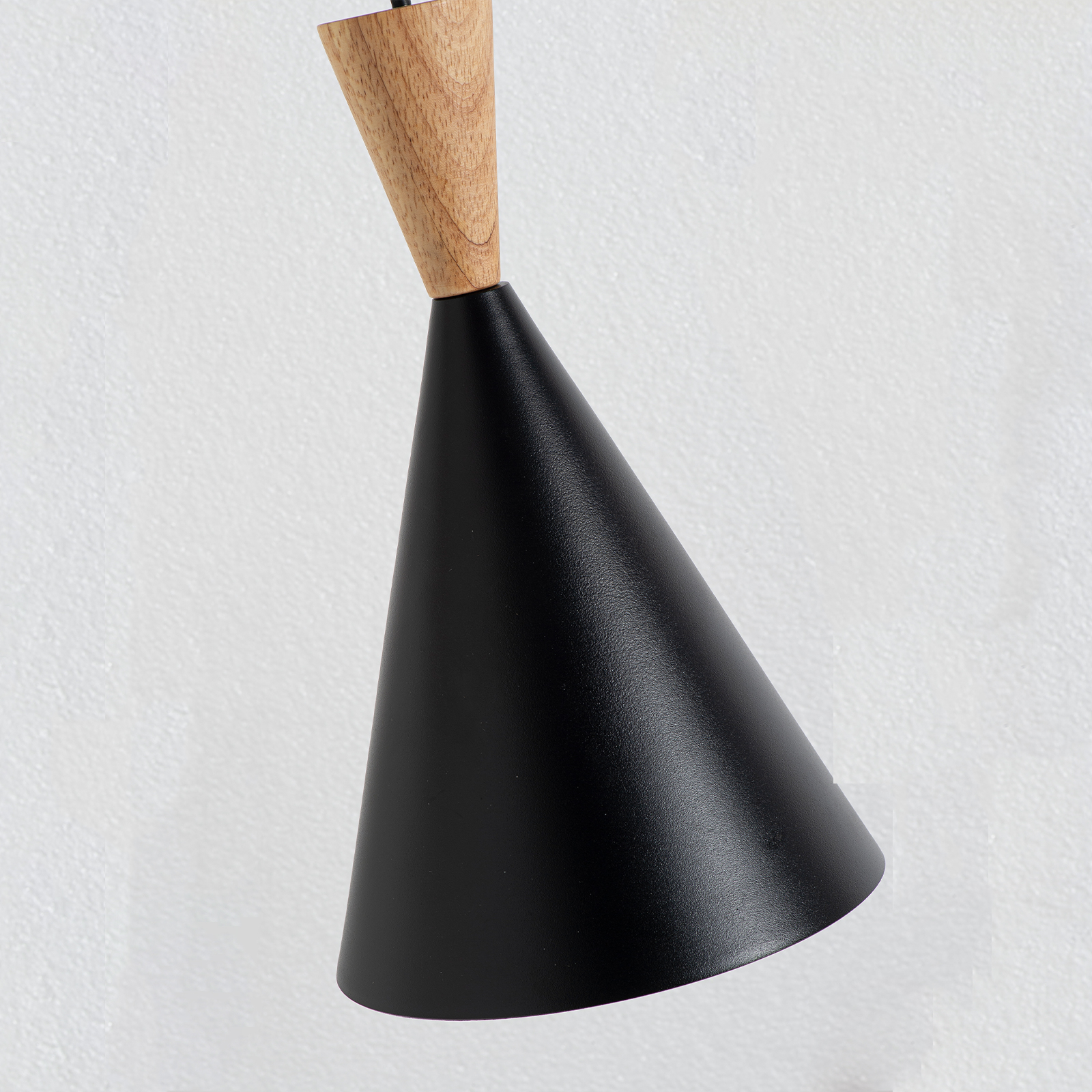 Lámpara negra cónica con vástago de madera, sobre fondo blanco texturizado.