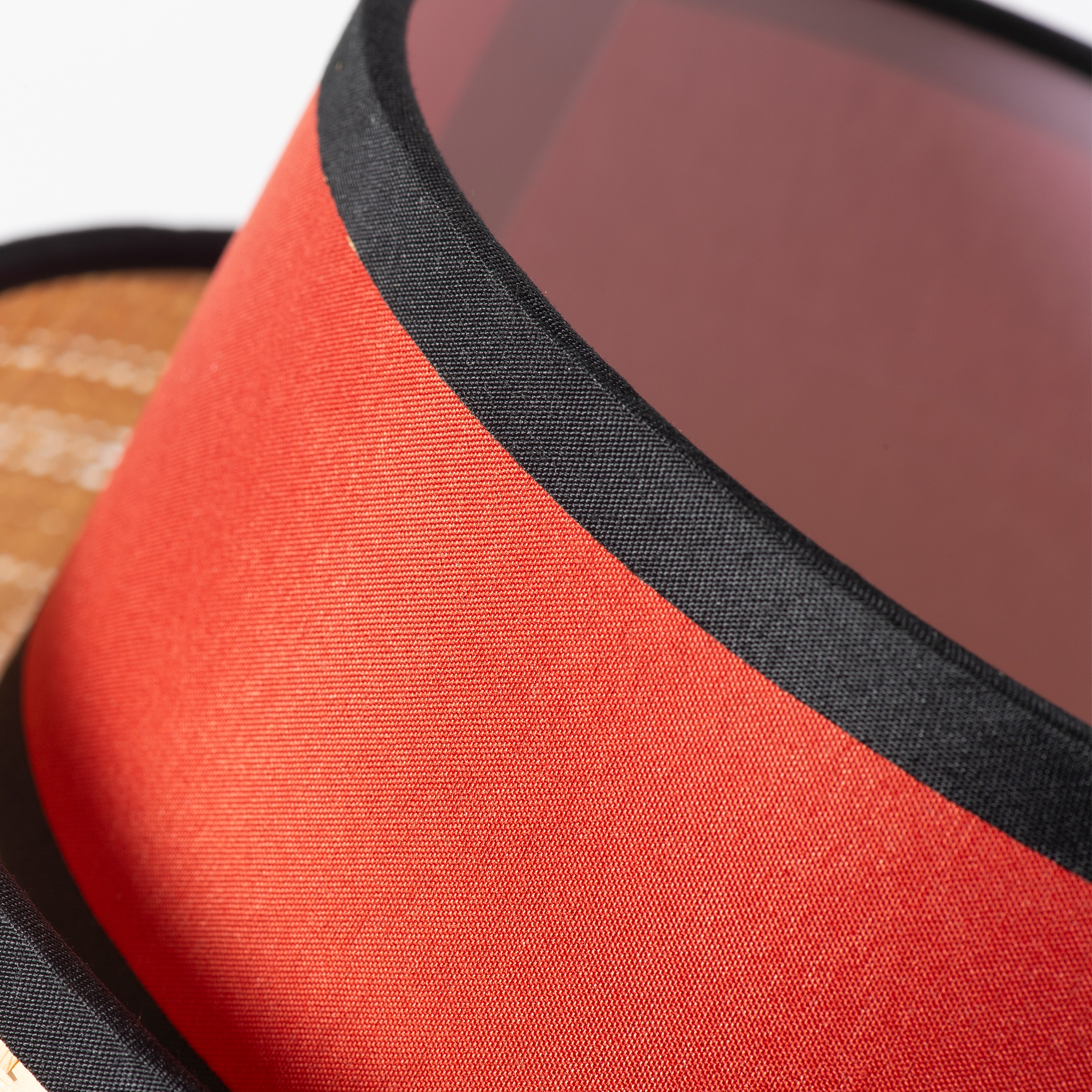 Una pantalla de lámpara roja con borde negro y parte de una cesta detrás.