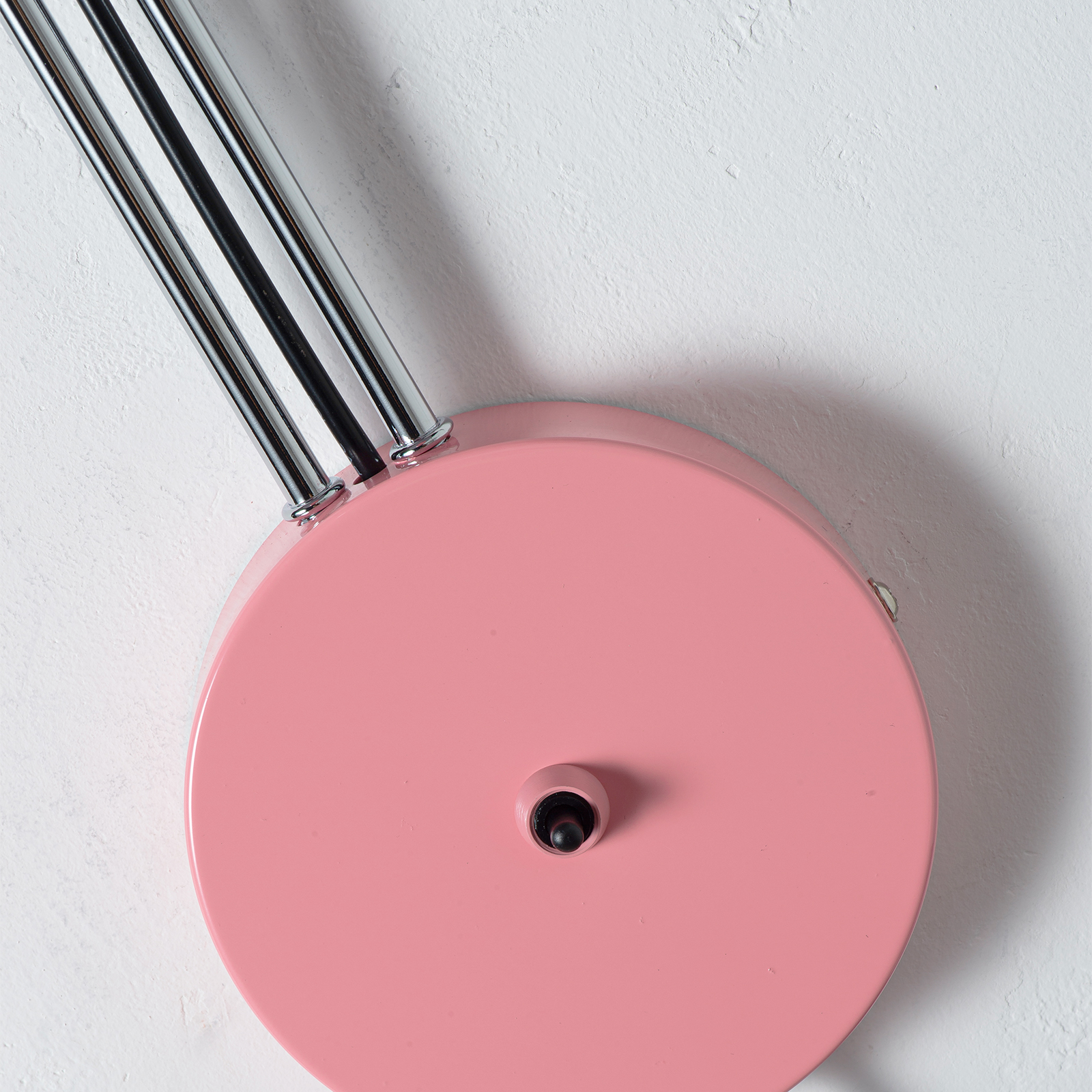 Una pantalla de lámpara rosa con brazos plateados contra una pared blanca.