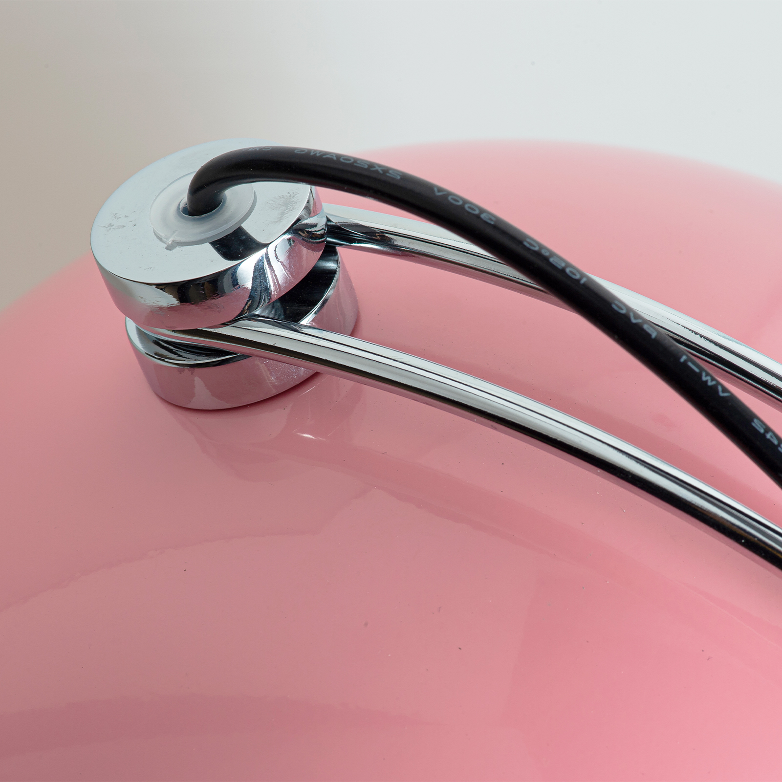 Primer plano de una lámpara rosa con detalles cromados y cable negro.