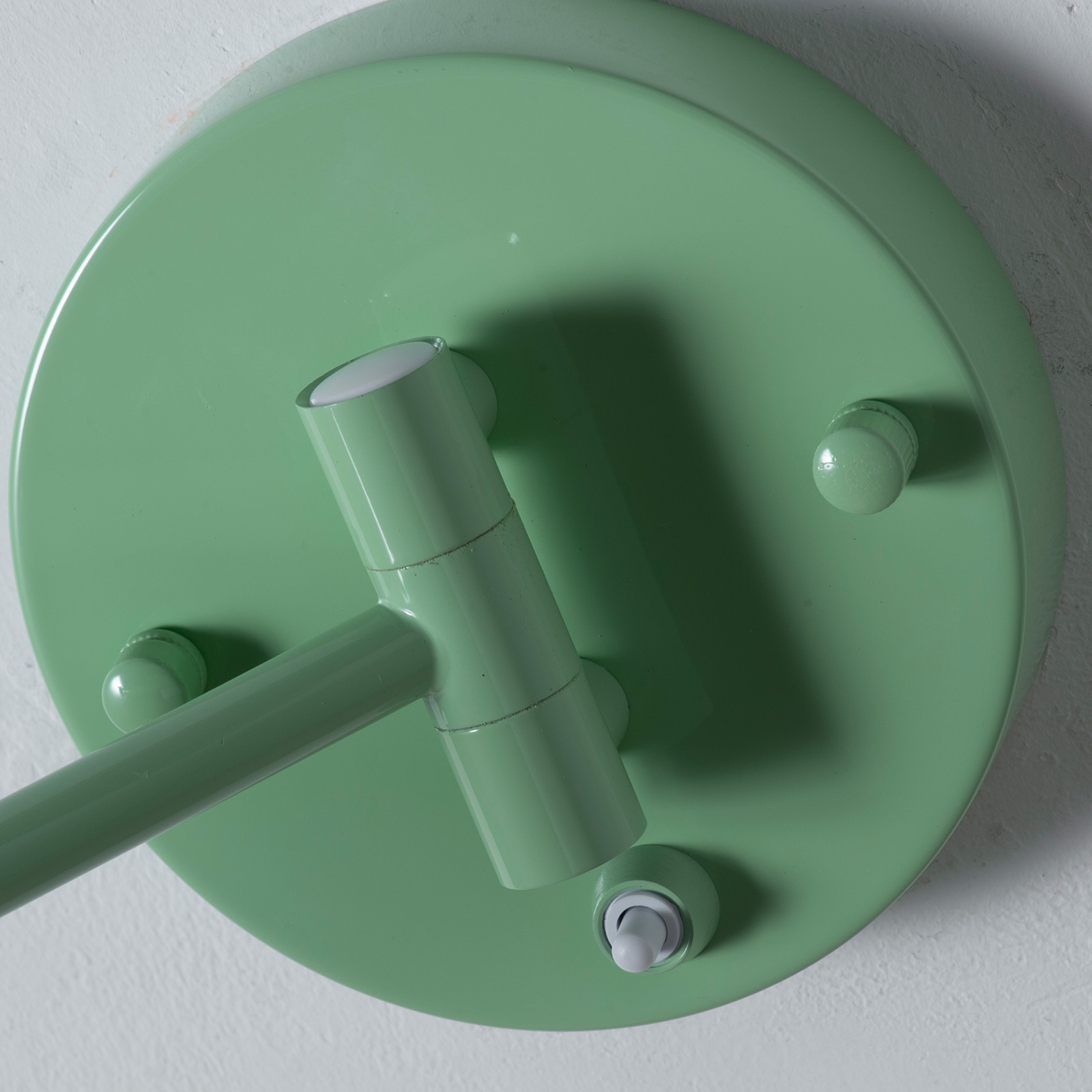 Lámpara de pared verde con brazo ajustable y interruptor en base redonda.