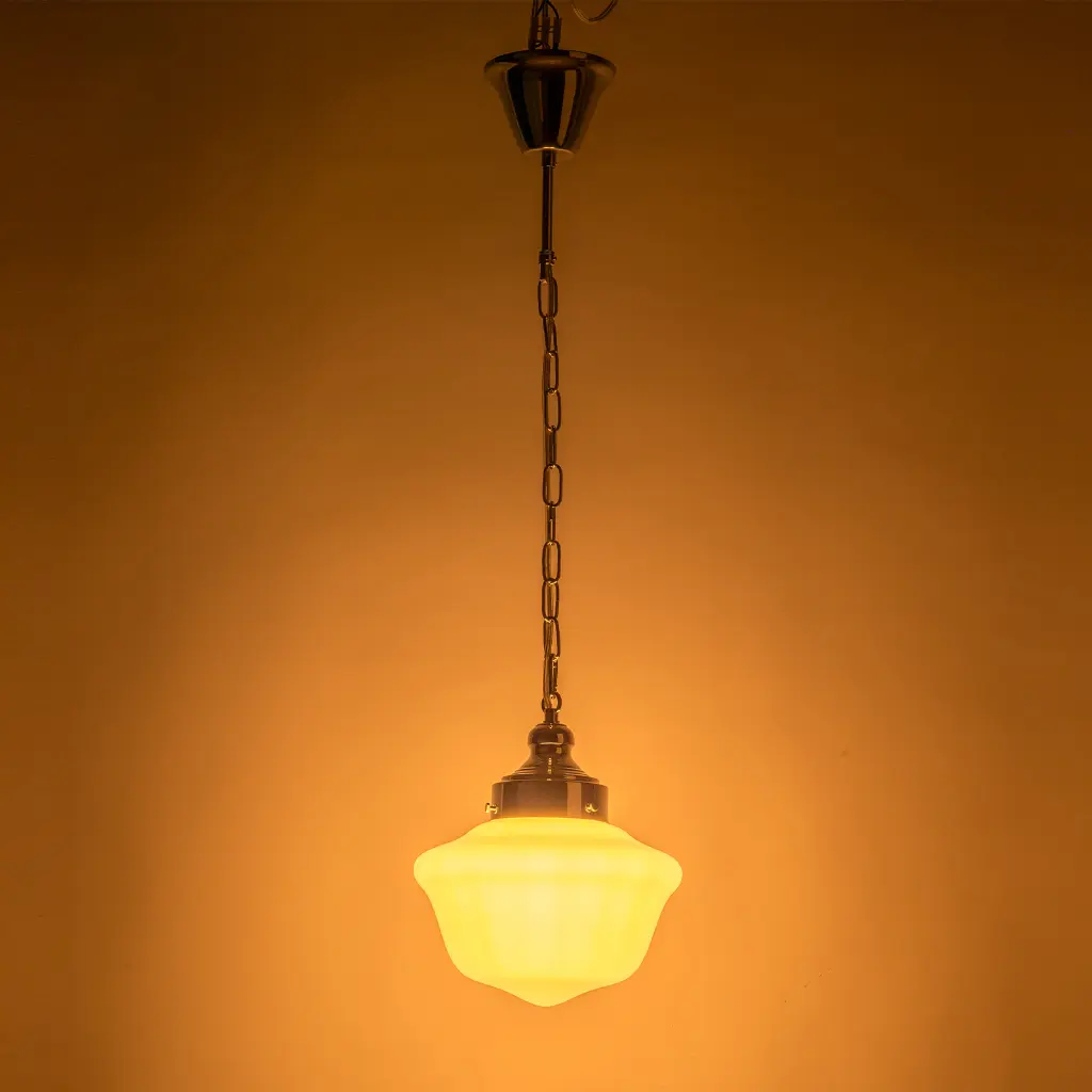 Una lámpara colgante con pantalla de cristal lechoso y cadena metálica brilla sobre fondo naranja.