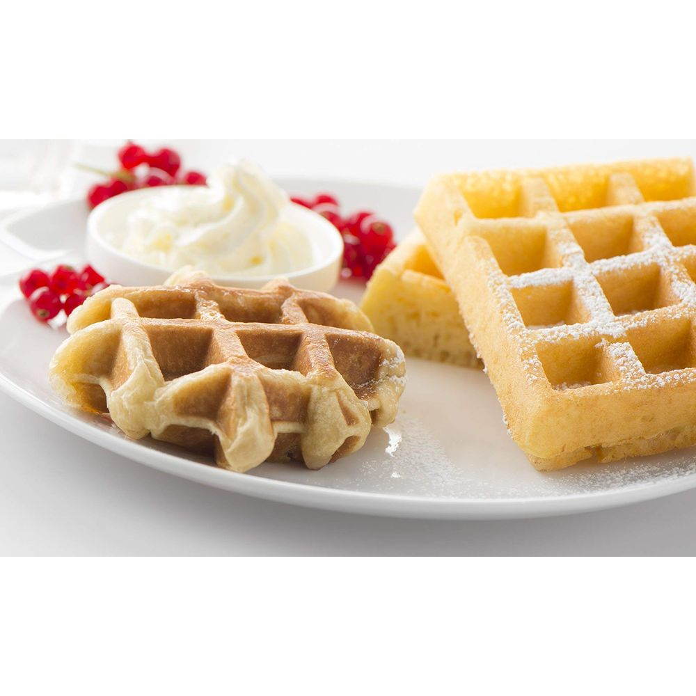 Due waffle con zucchero a velo, bacche e panna montata su un piatto.