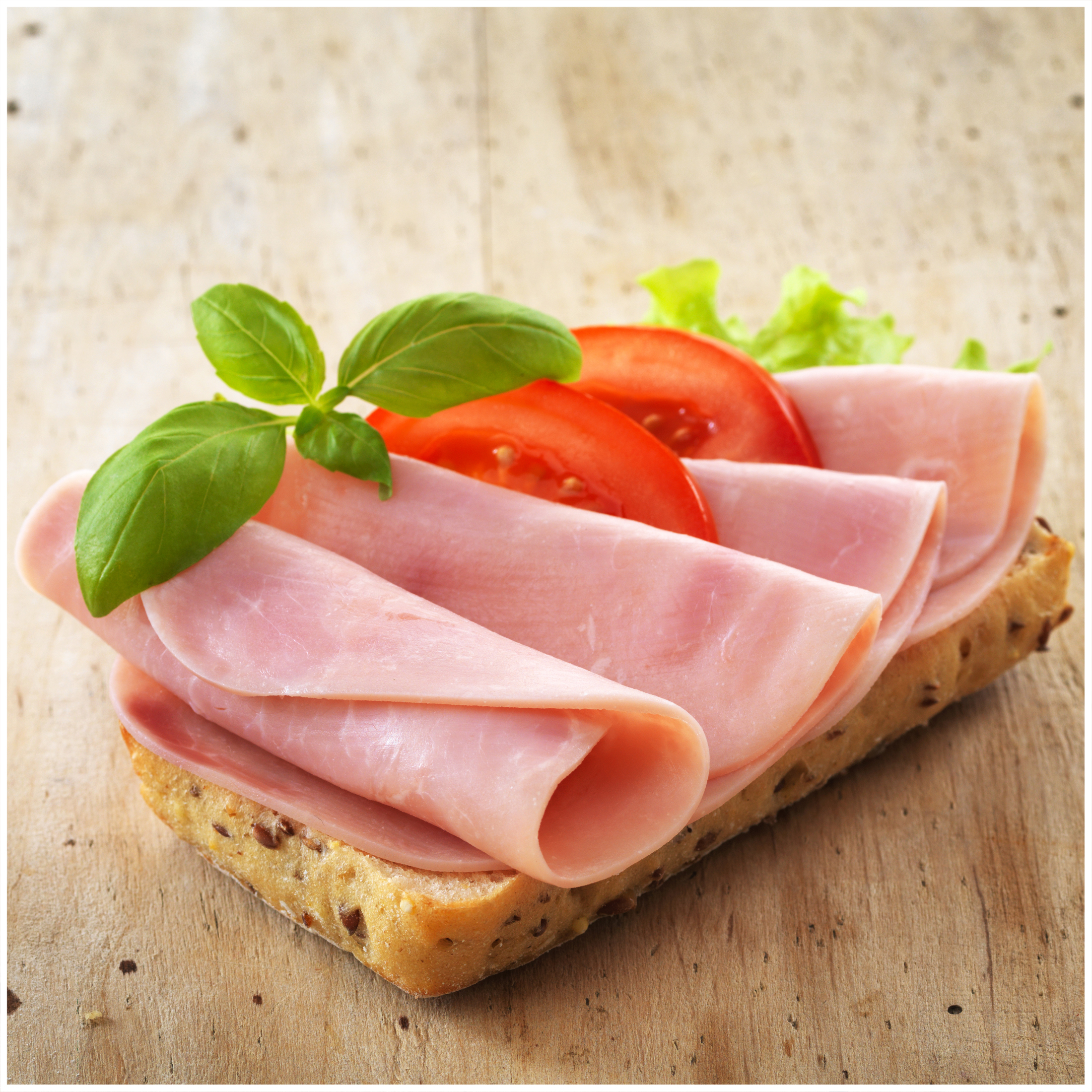 Un panino con prosciutto, pomodoro, lattuga e basilico su legno.