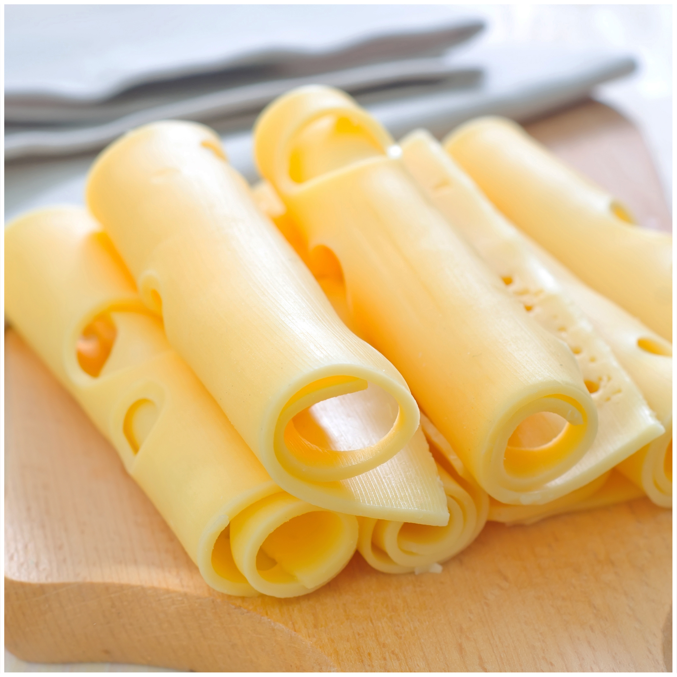 Formaggio giallo arrotolato con buchi su tagliere di legno.