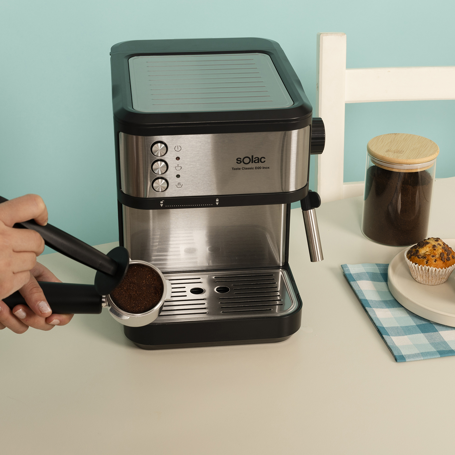 Una persona prepara café con una máquina de espresso, con un muffin y posos de café cerca.