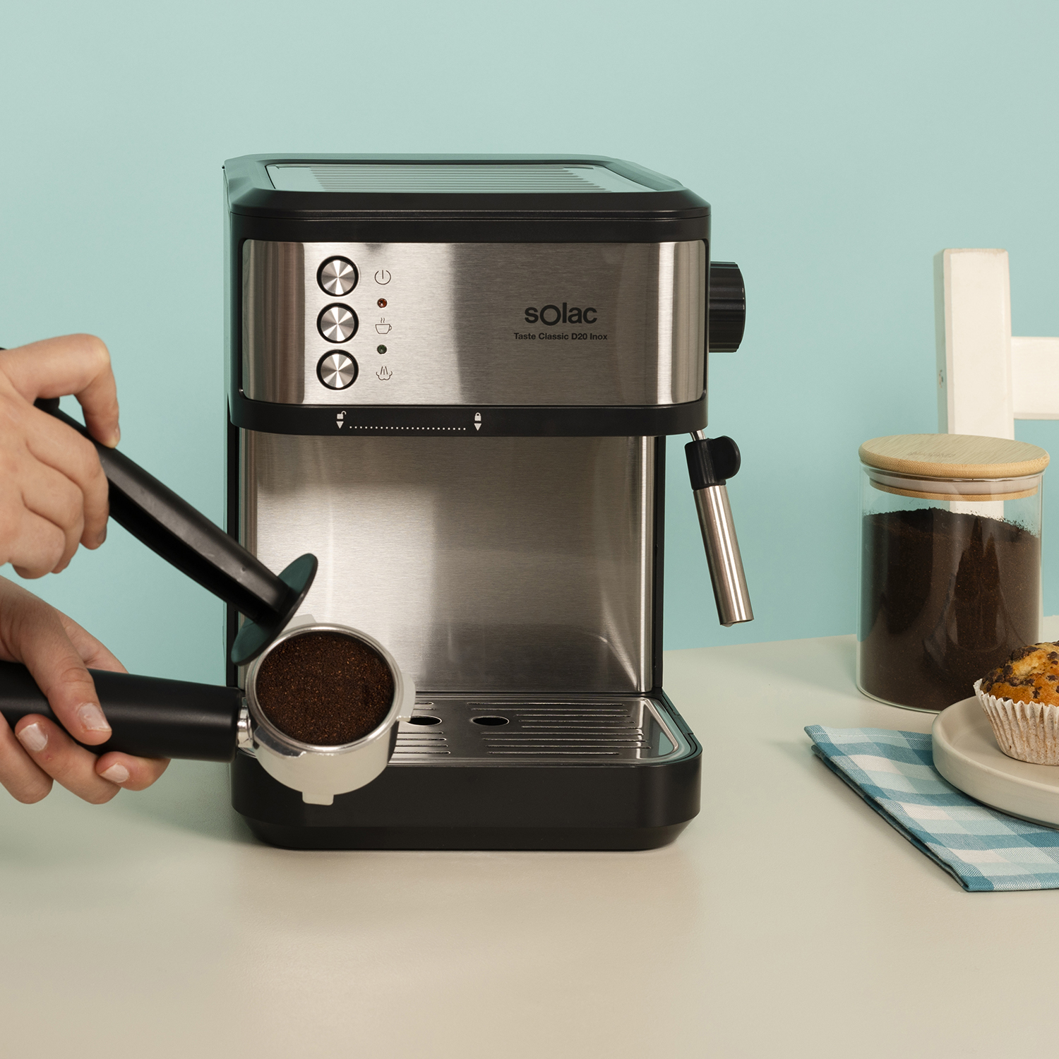 Máquina espresso de acero inoxidable con portafiltro, tarro de café y muffin.