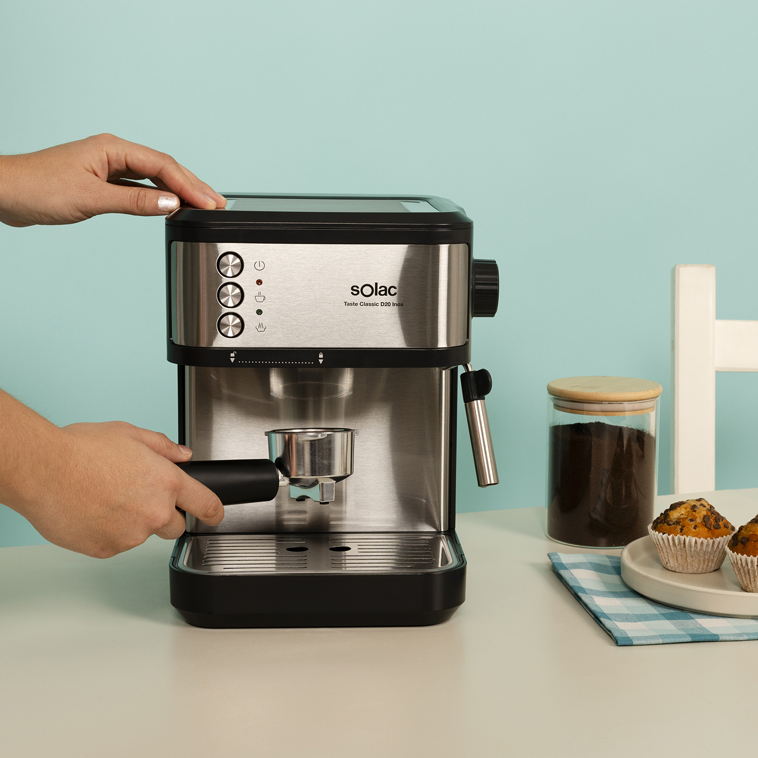 Una mano opera una cafetera, con muffins y posos de café cerca.