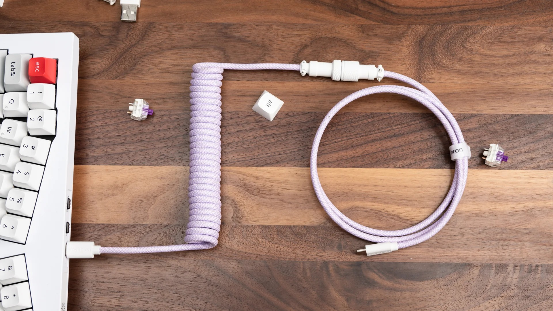 Biała klawiatura, fioletowy kabel i dwa przełączniki na drewnie.