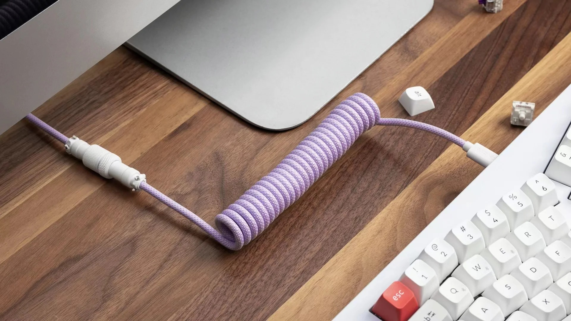 Fioletowy kabel w kształcie spirali z białymi złączami na drewnianym biurku obok klawiatury.