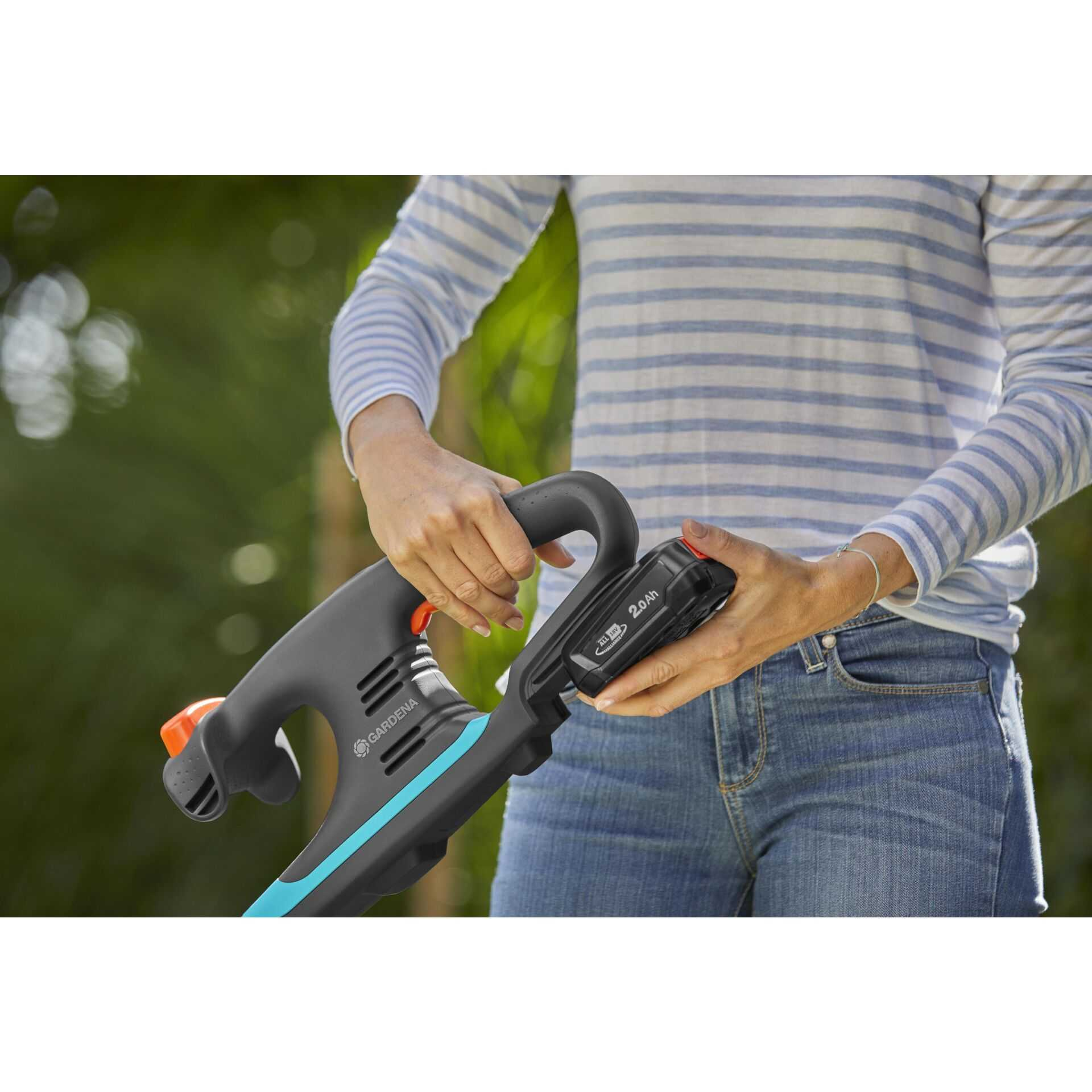 Una donna con maglia a righe inserisce una batteria in un attrezzo da giardino.