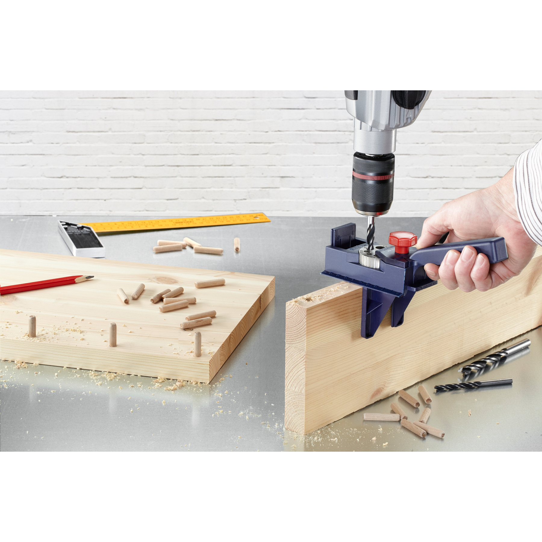 Holzdübel und Bohrwerkzeug auf Werkbank mit Holz und Maßband.