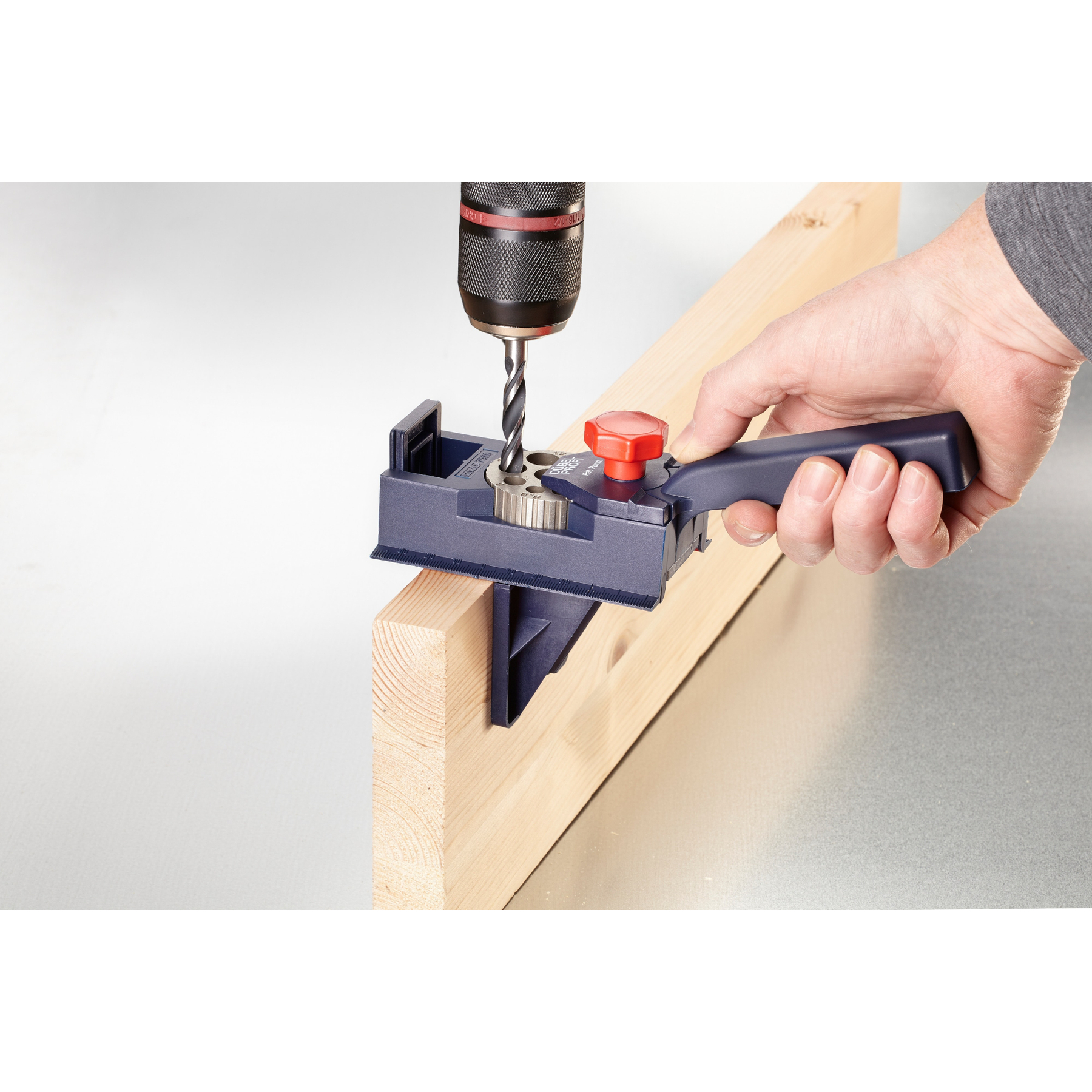 Bohrer mit Dübelvorrichtung bohrt in Holz. Hand hält Griff. Grauer Hintergrund.