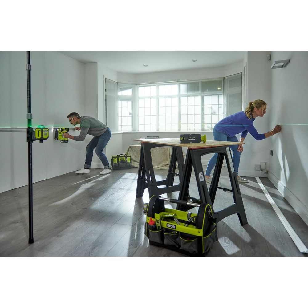 Mann und Frau arbeiten an Wänden mit grünen Laserlinien. Werkzeugkasten auf Böcken.