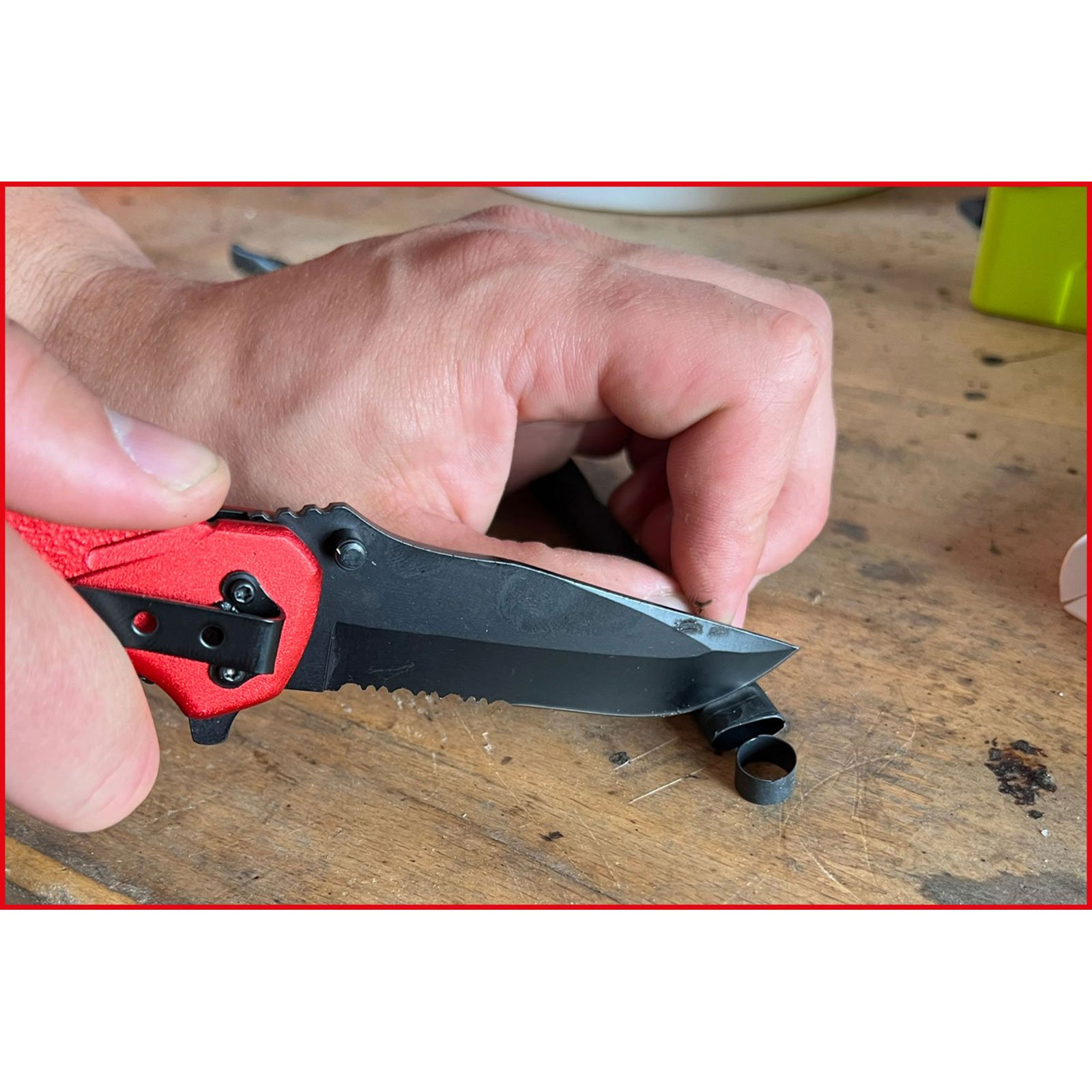 Eine Hand benutzt ein rotes Klappmesser, um ein kleines schwarzes Ringteil zu schneiden.