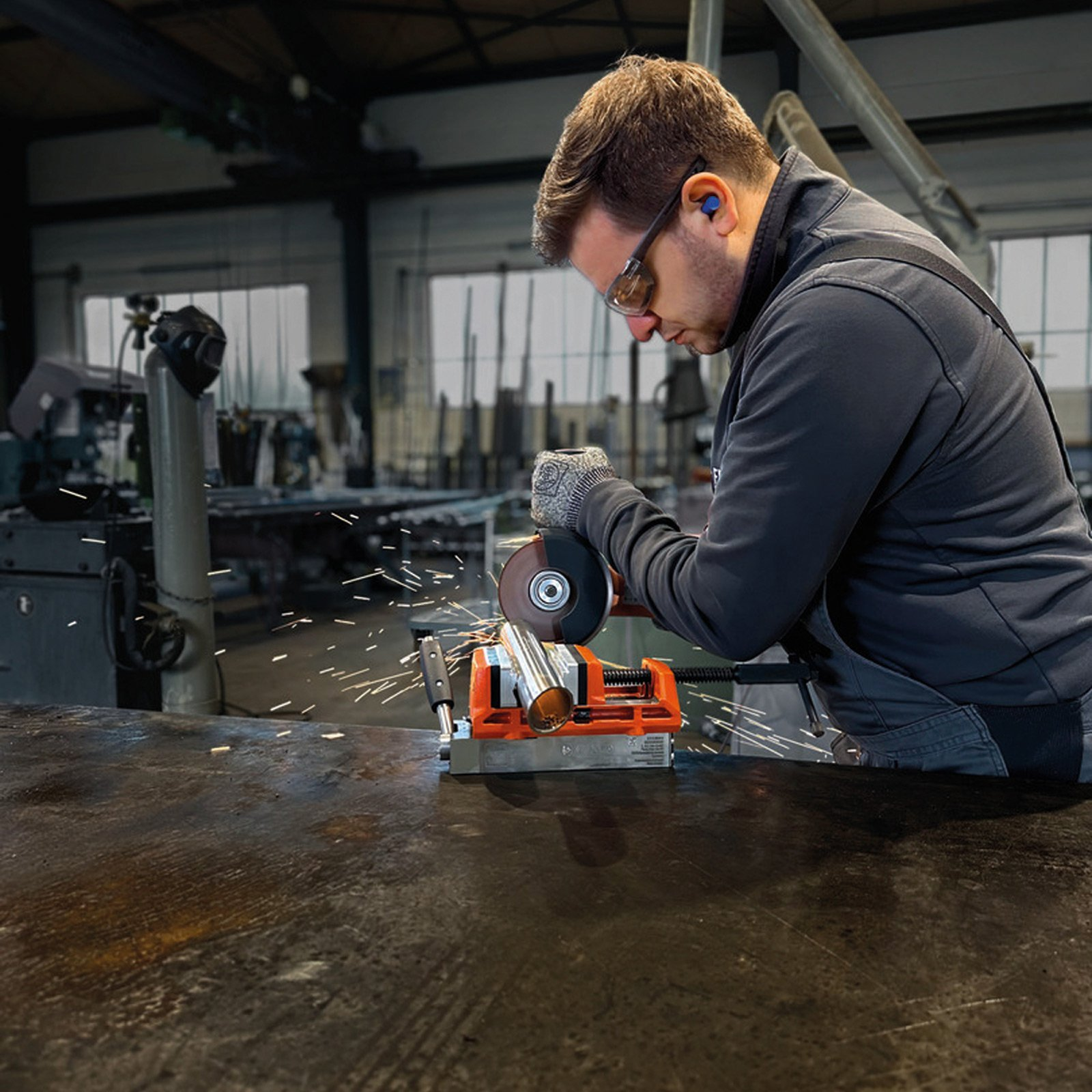 Mann mit Schutzbrille schneidet Metallrohr mit Winkelschleifer, Funken fliegen.
