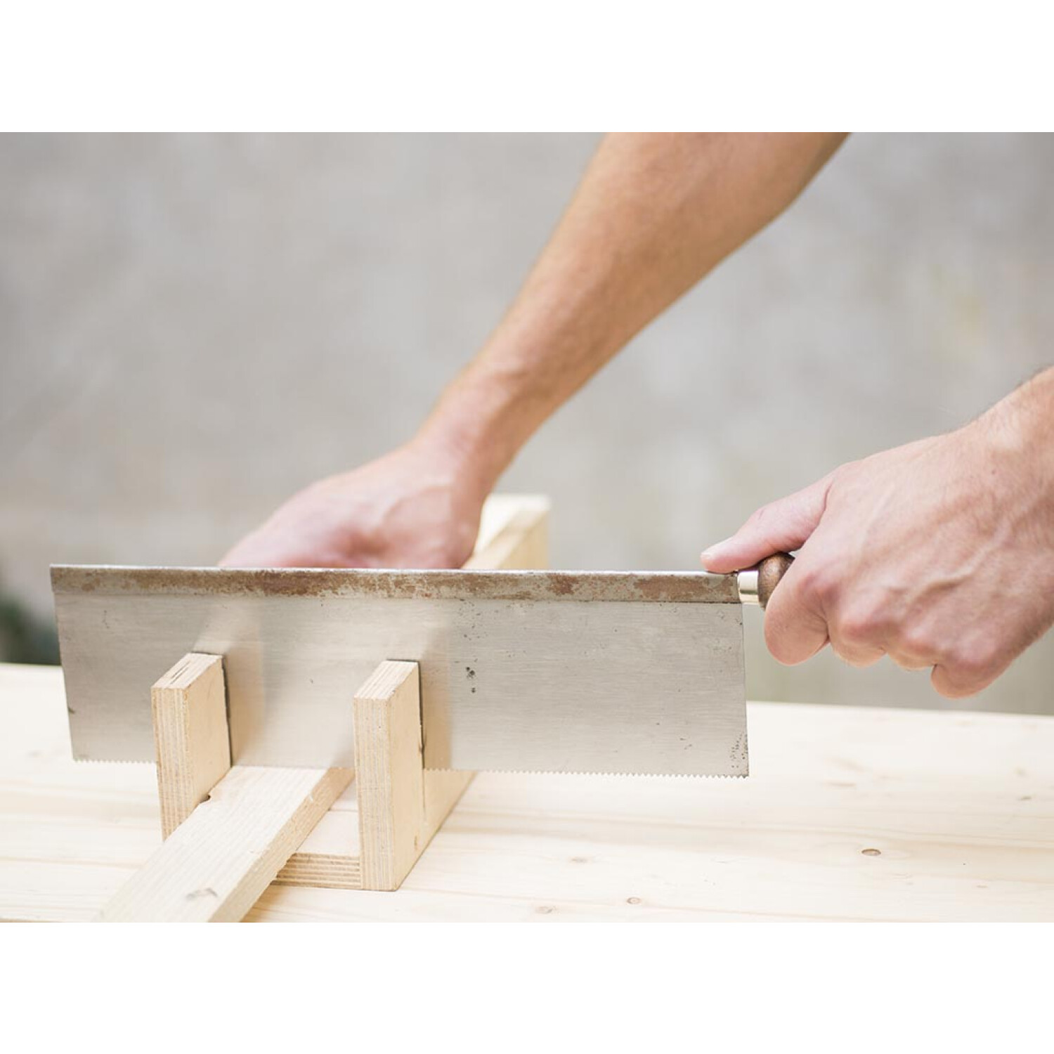 Hände sägen Holz mit einer Handsäge, die auf einem Holzstück ruht.