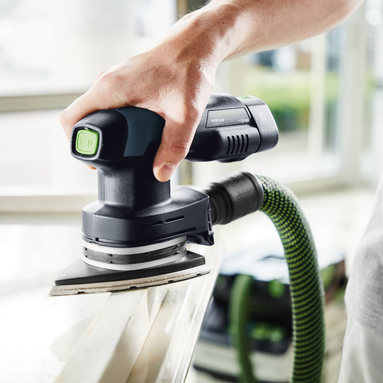 Hand hält Schleifmaschine, die Holz bearbeitet. Grüne und schwarze Maschine mit Schlauch.