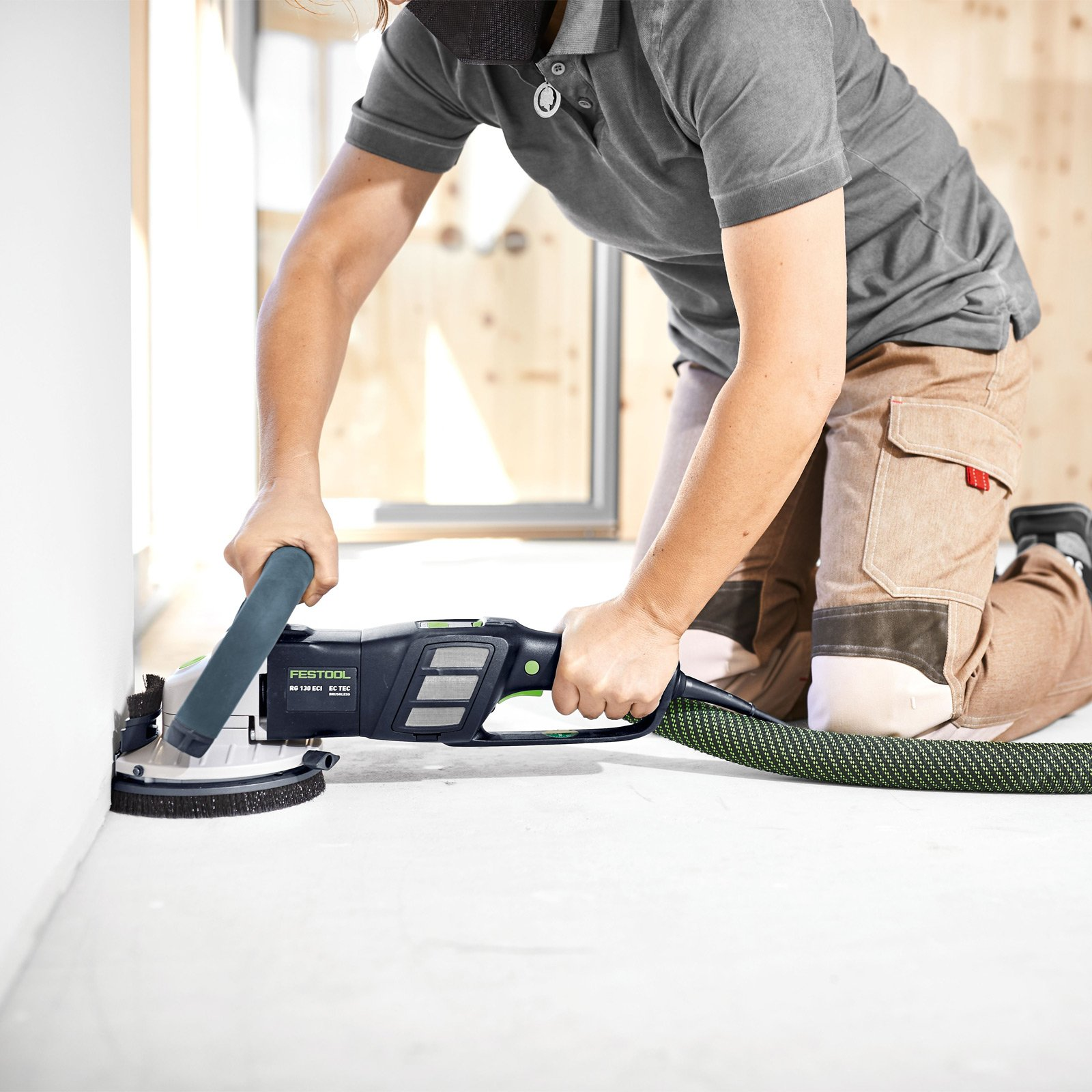 Person schleift Wandkante mit Festool Schleifmaschine, Knieend auf dem Boden.