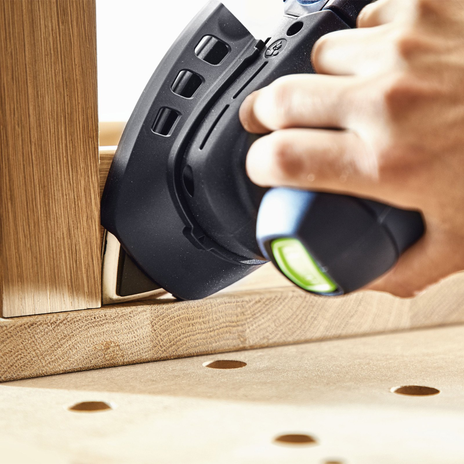 Hand schleift Holz mit schwarzem Werkzeug und grüner Lampe.