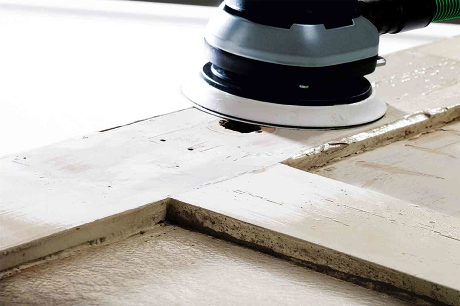 Ein Schleifgerät bearbeitet eine weiße Holztür. Staub wird aufgewirbelt.