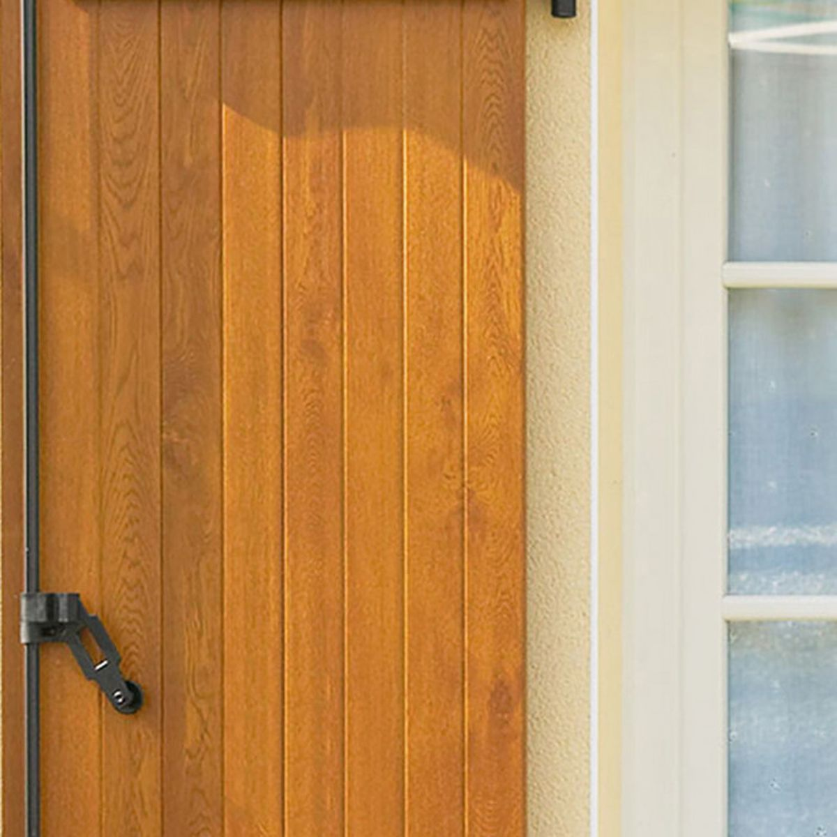 Holztür mit schwarzem Riegel und Fenster daneben.