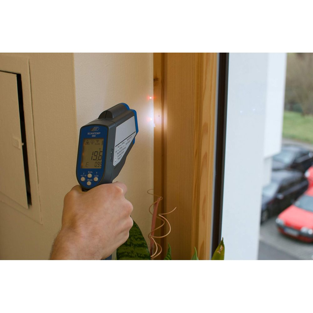 Ein Mann misst die Temperatur einer Wand mit einem Infrarotthermometer. Autos draußen.