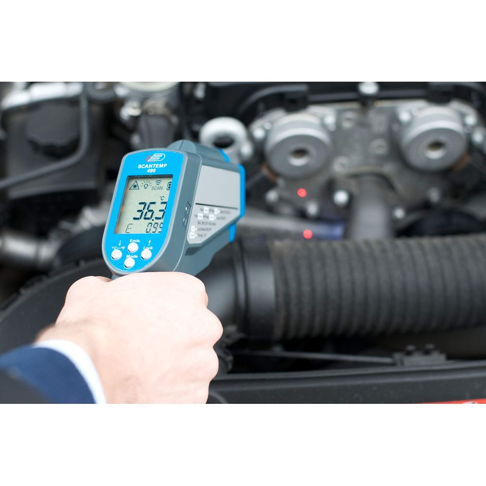 Eine Hand hält ein Infrarotthermometer vor einem Fahrzeugmotor.
