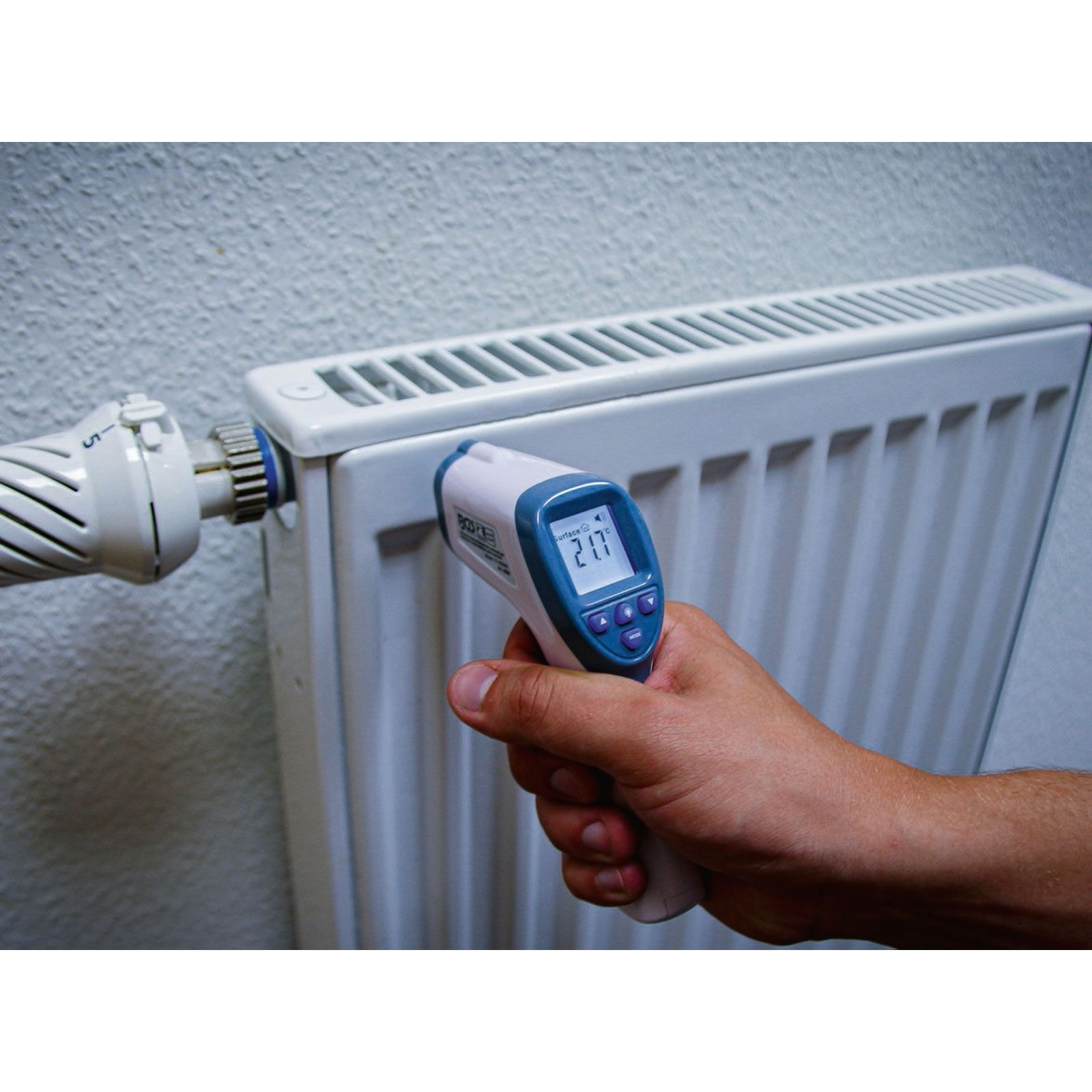 Ein Mann misst mit einem Infrarotthermometer die Temperatur eines Heizkörpers.