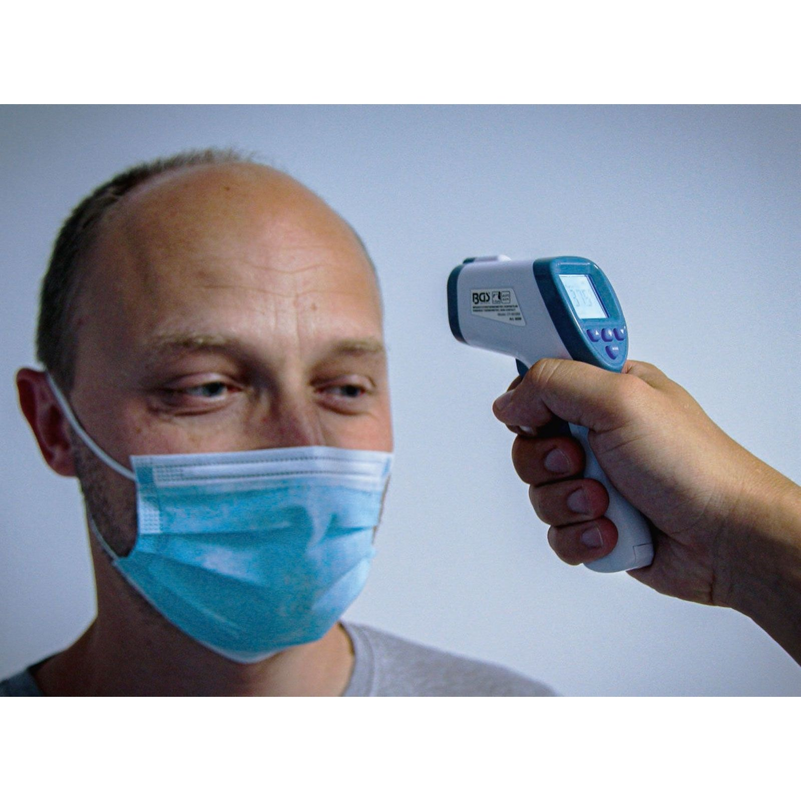 Ein Mann mit Maske wird mit einem Fieberthermometer gemessen.