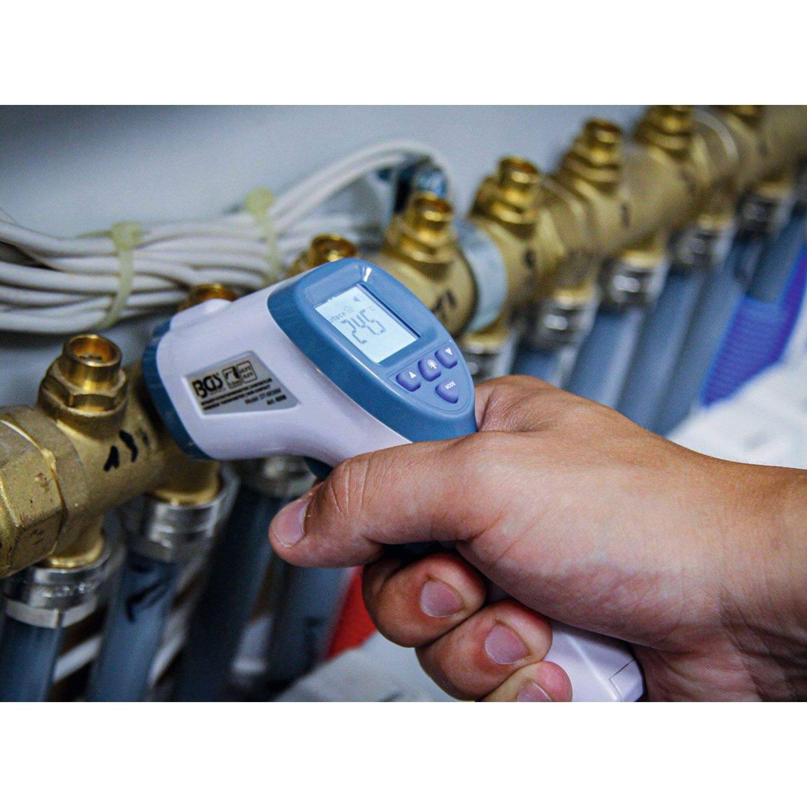 Ein Mann misst mit einem Infrarotthermometer die Temperatur von Rohren.