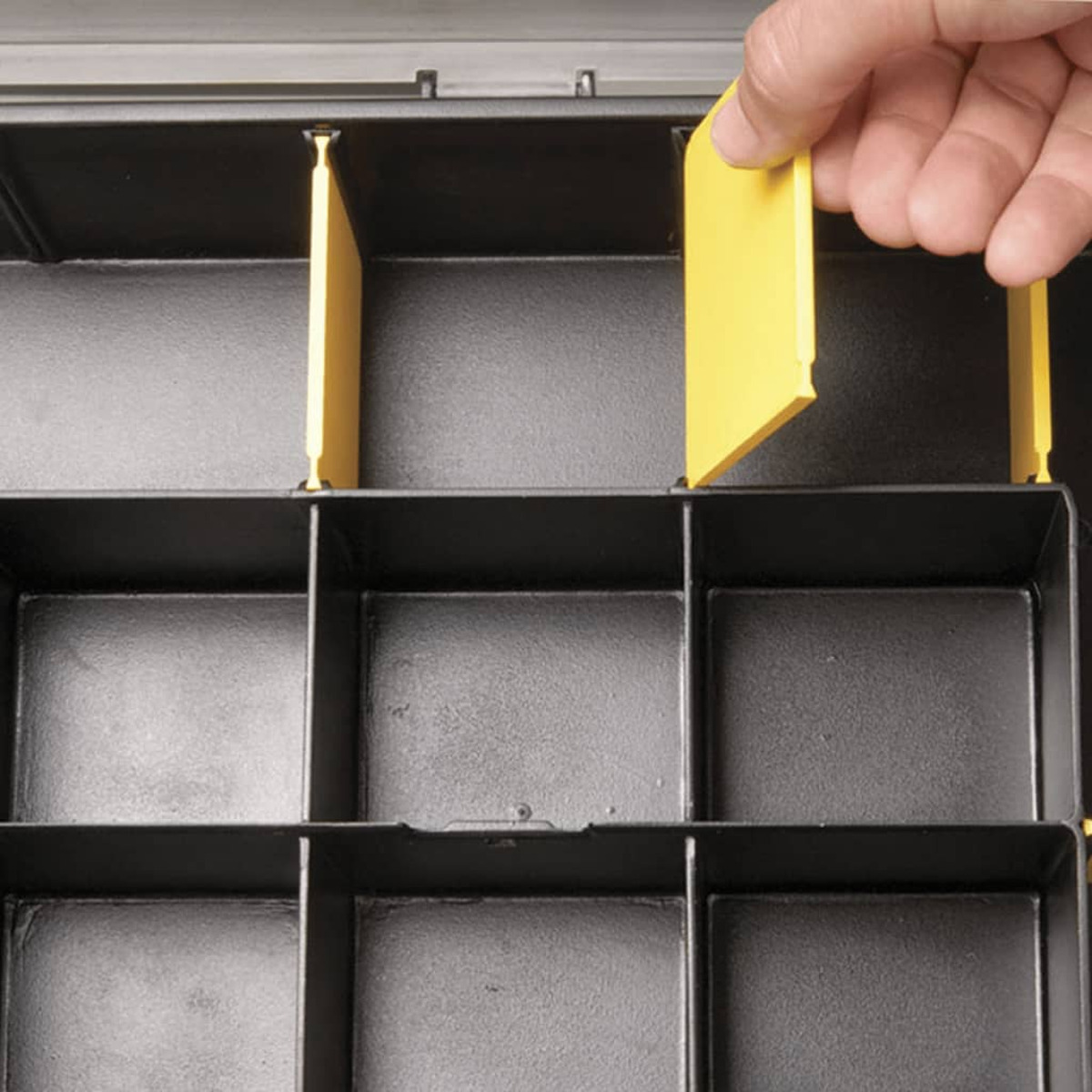 Una mano posiziona un divisorio giallo in un organizer nero con scomparti.