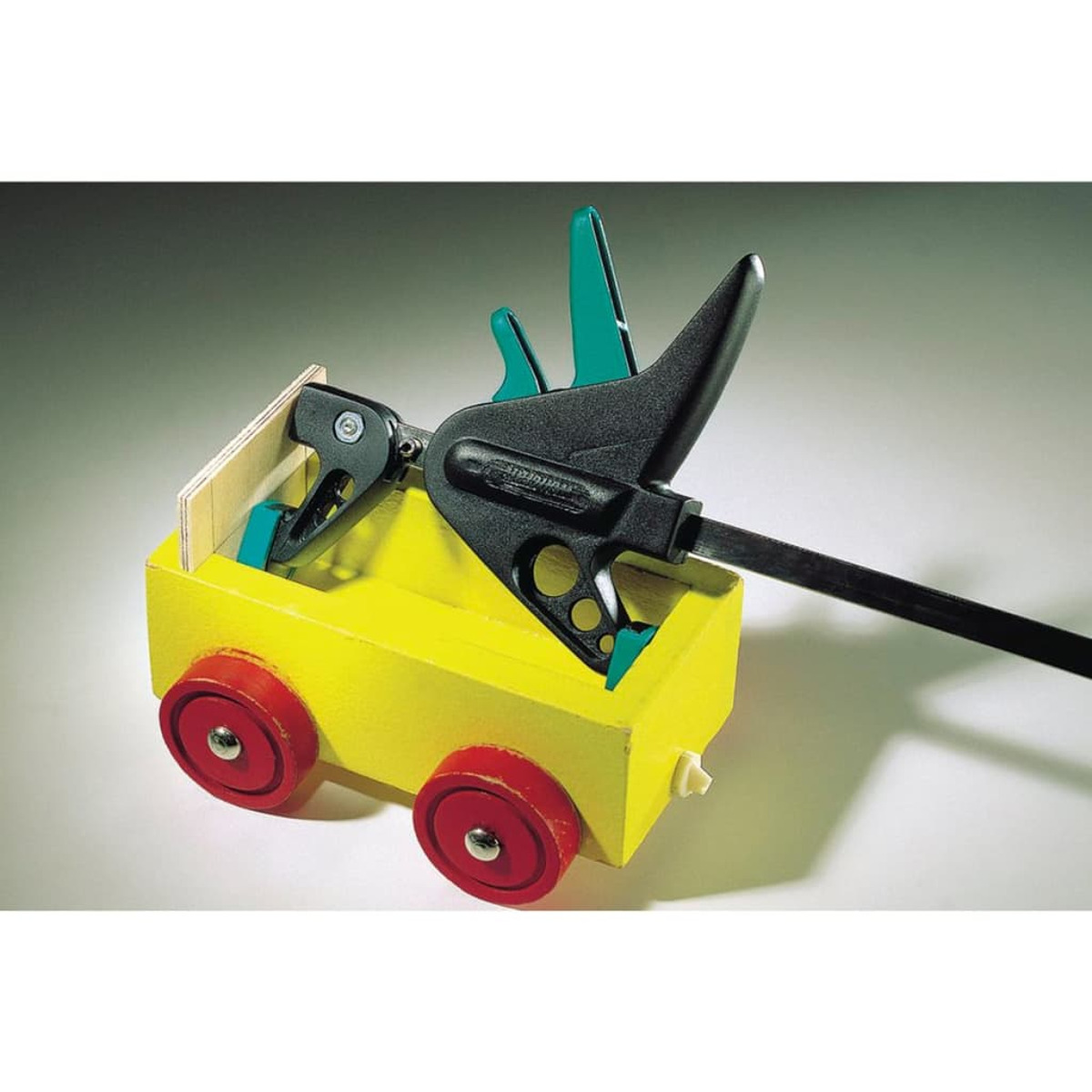 Ein gelber Holzwagen mit roten Rädern wird von einer schwarzen Zwinge gehalten.