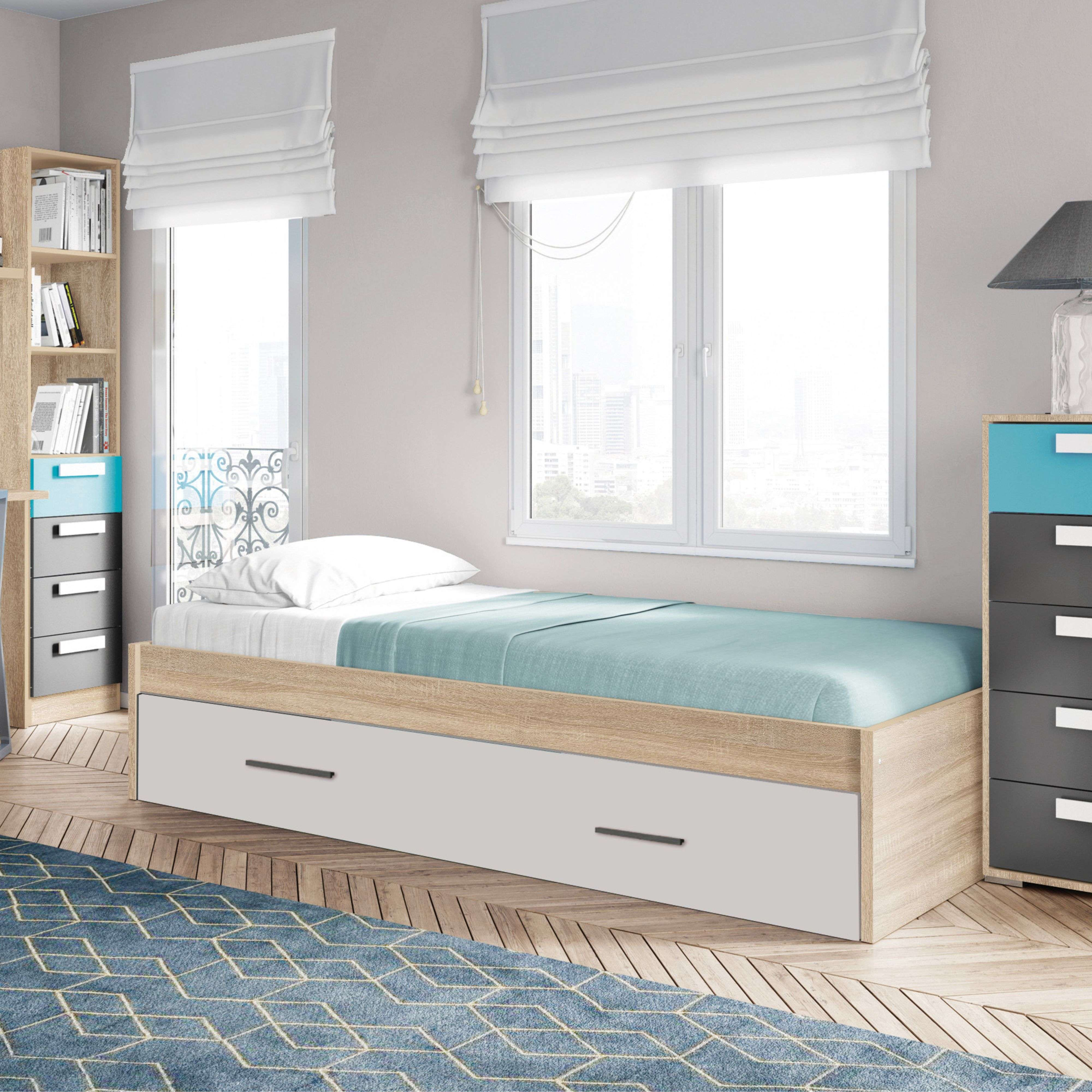 Una cama individual con manta azul y almohada blanca sobre suelo de madera con alfombra.
