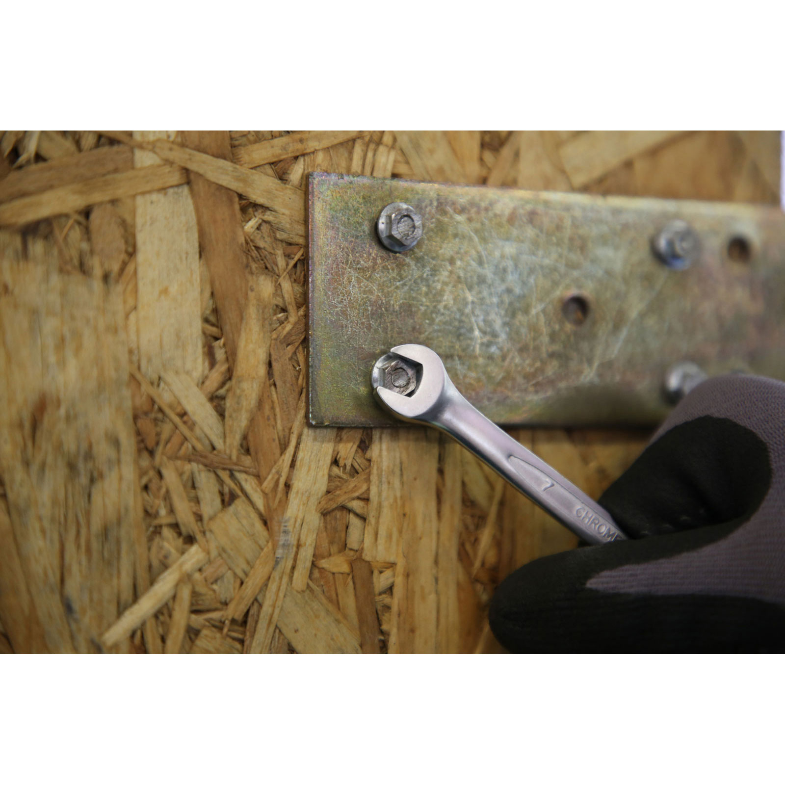 Eine Hand mit Handschuh benutzt einen Schraubenschlüssel, um eine Schraube an einer Metallplatte zu befestigen.