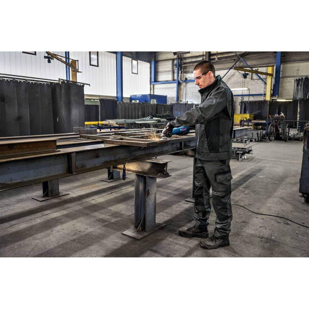 Mann schleift Metall mit Winkelschleifer in Fabrik, Funken fliegen.