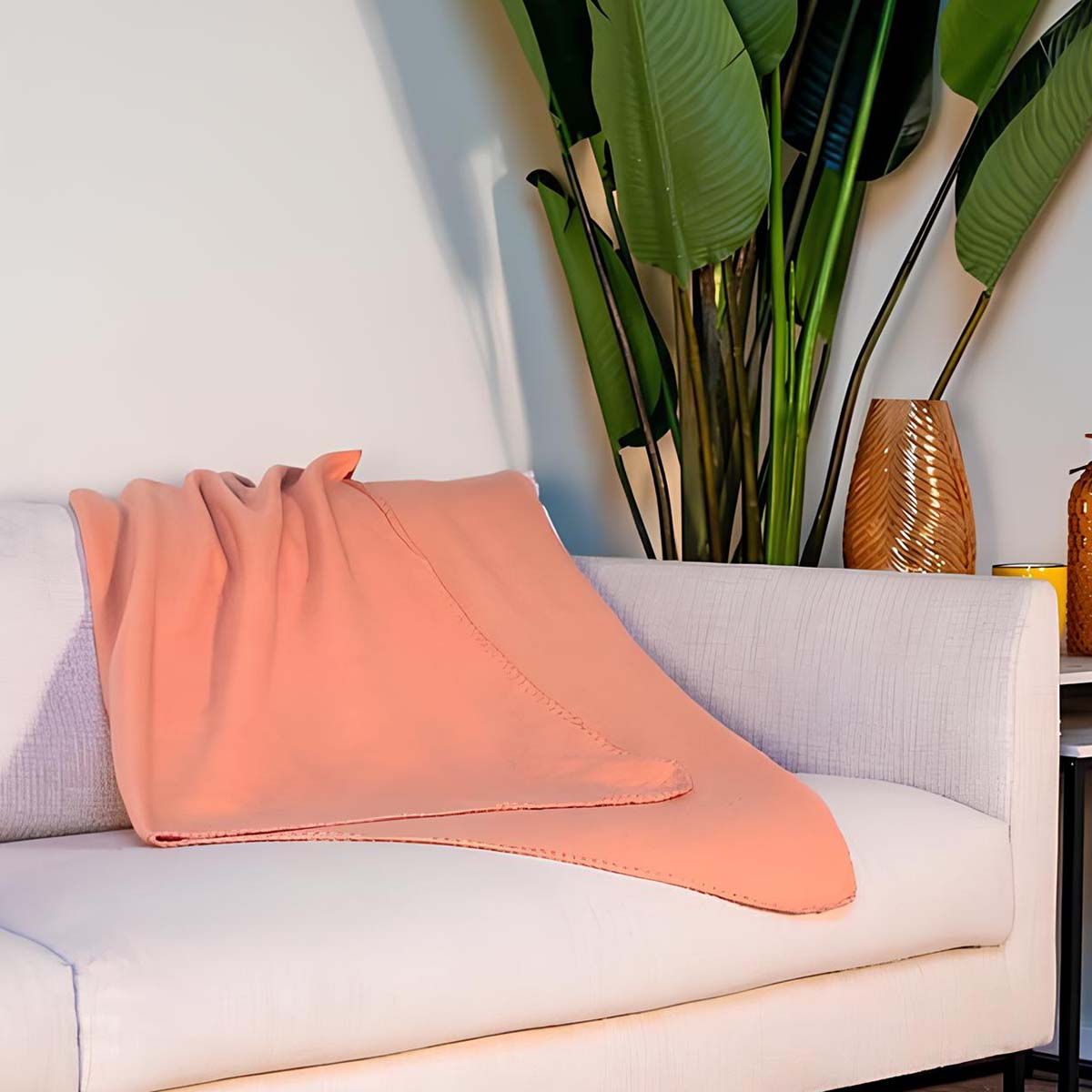 Una coperta color corallo è drappeggiata su un divano bianco accanto a una grande pianta.