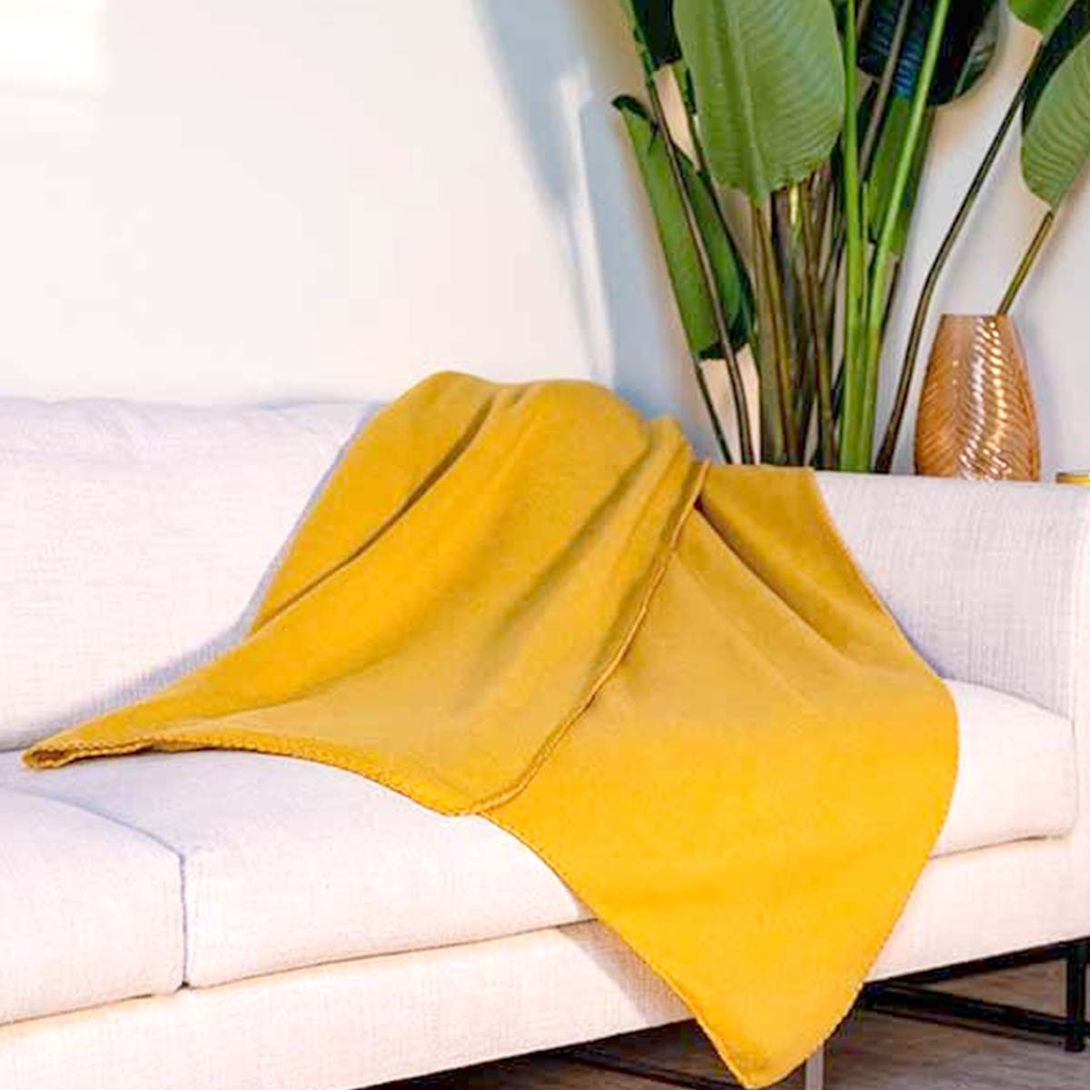 Una coperta gialla è drappeggiata su un divano bianco accanto a una pianta in vaso e un vaso.