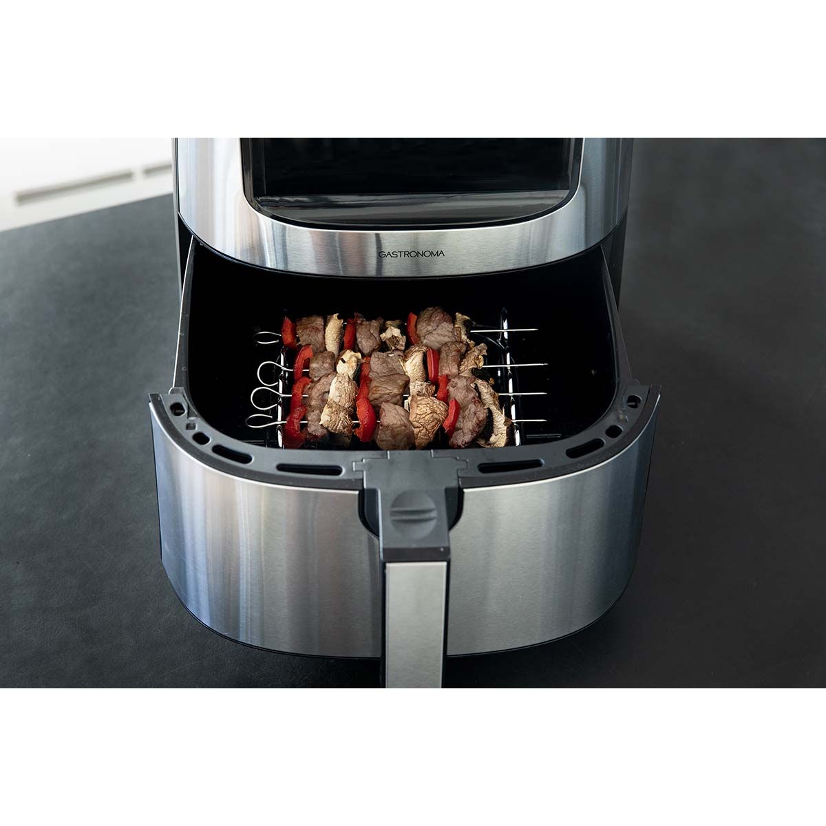 Vleesspiesen met paprika en champignons op een rooster in een airfryer.