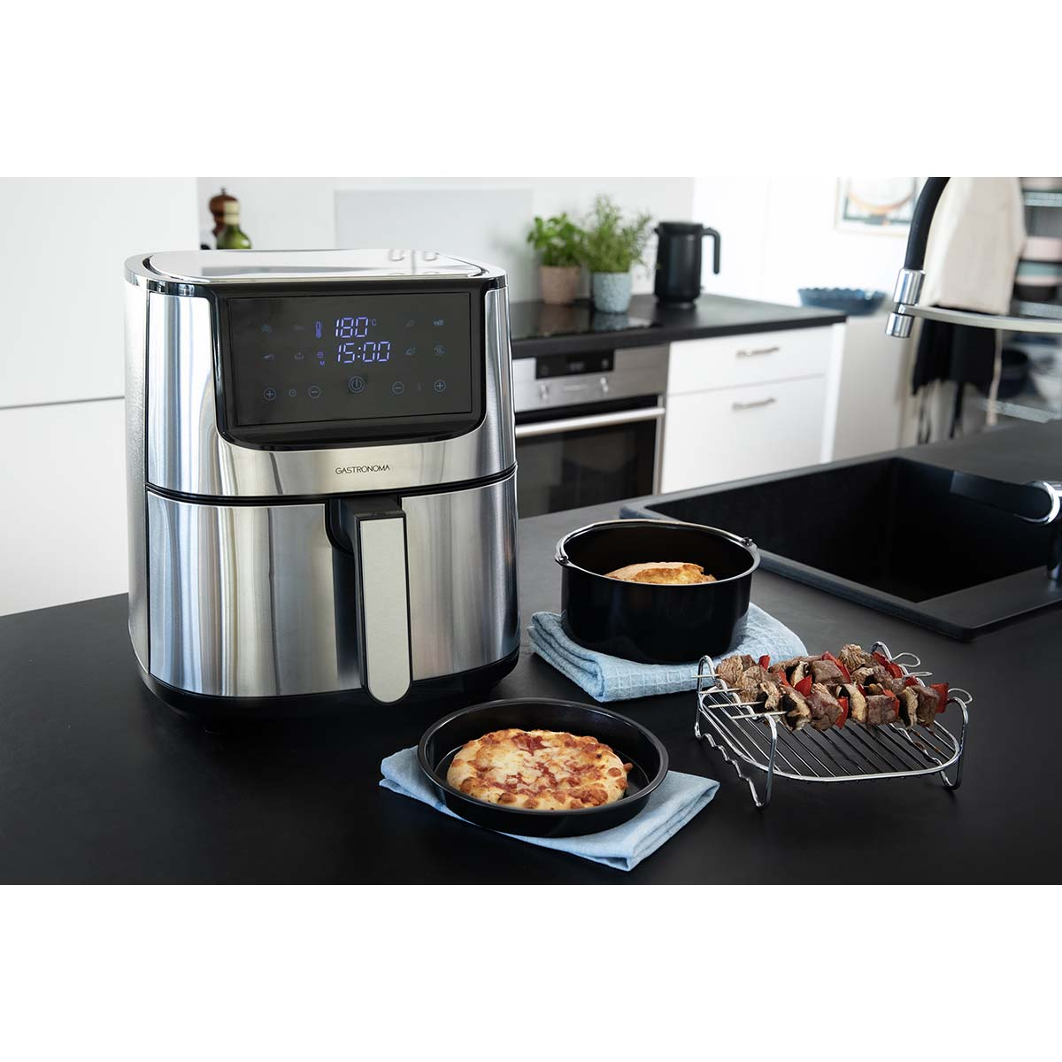 Roestvrijstalen airfryer met digitaal display, ernaast een mini pizza, een gebraden kip en vleesspiesen.