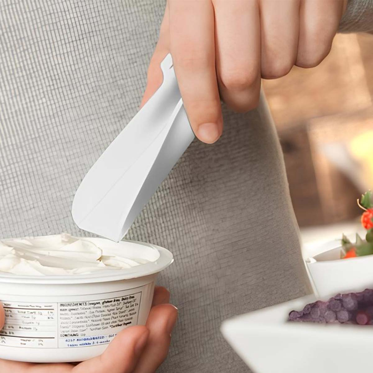 Una persona usa un mestolo bianco per prendere il formaggio cremoso da una vaschetta. Ci sono delle bacche in una ciotola vicina.