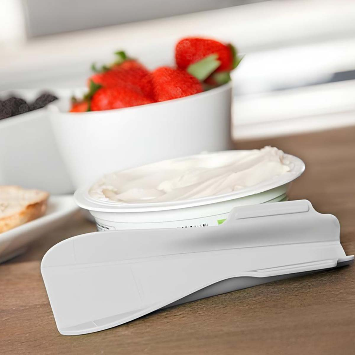 Un dispenser bianco per formaggio cremoso accanto a una ciotola di fragole.
