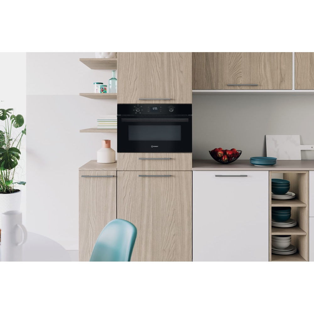 Cucina moderna con forno da incasso, elementi in legno e ciotola di frutta.