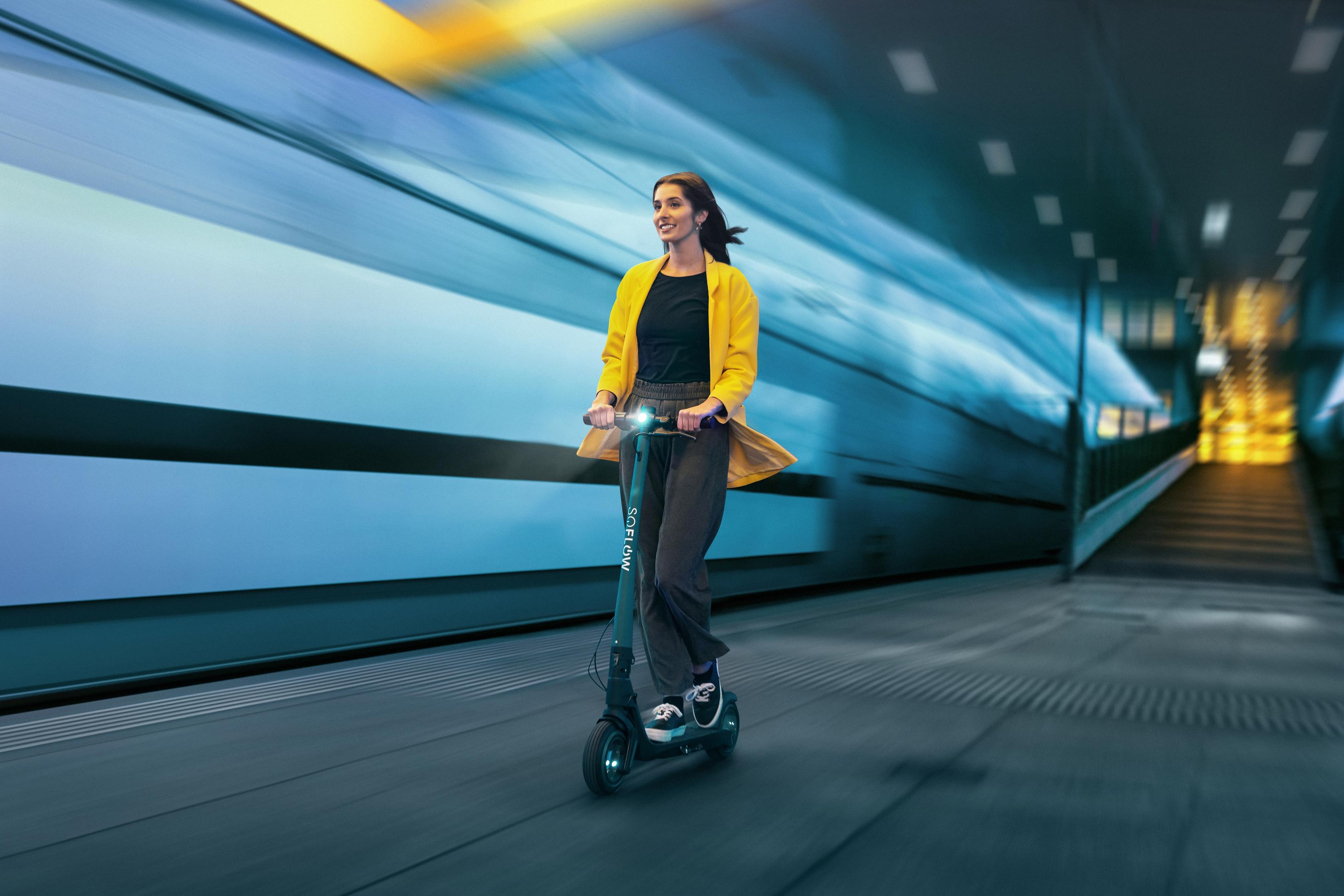 Eine Frau fährt einen E-Scooter in einem modernen Tunnel mit blauen und gelben Lichtern.