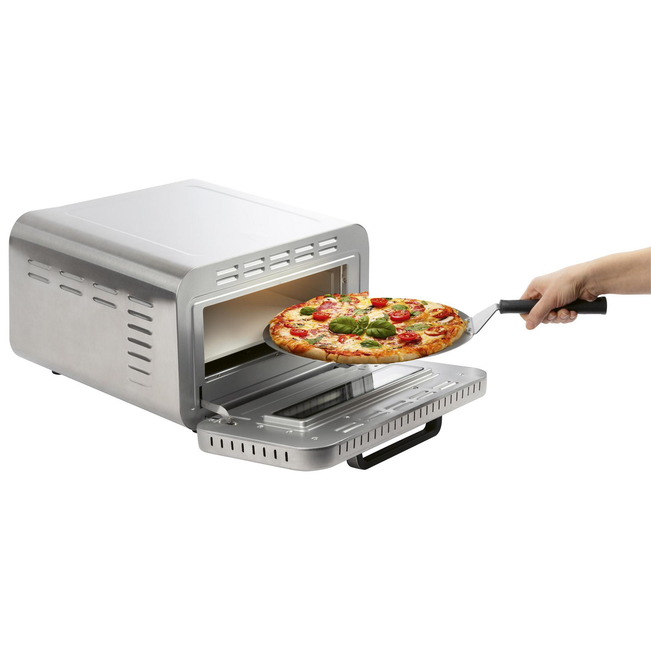 Eine Hand schiebt eine Pizza mit Tomaten und Basilikum in einen Toasterofen.
