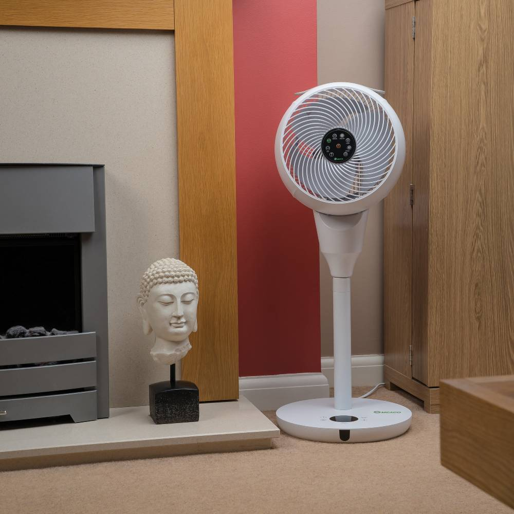 Un ventilador blanco junto a un busto de Buda y una chimenea sobre alfombra.