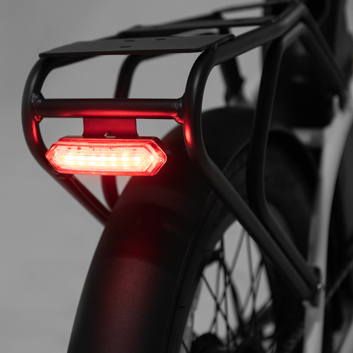 La luce posteriore rossa di una bicicletta è illuminata, mostrando ruota e portapacchi.